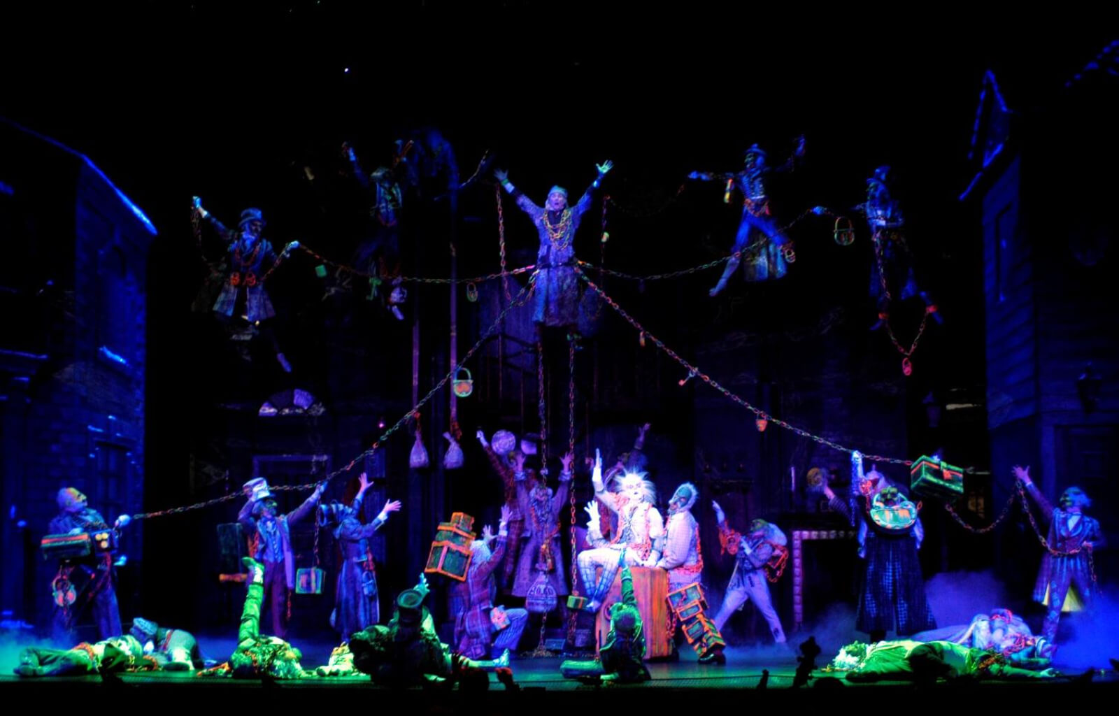 "Link by Link" in A Christmas Carol. Scrooge floats in the air and is visited by the ghost of Jacob Marley and a cast of spirits with blacklight affected costumes.