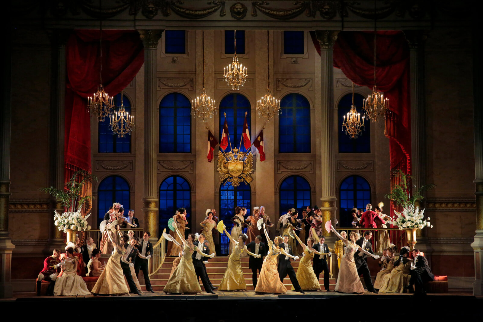 Ladies and gentlemen dancing in beautiful gold-themed dresses and black tux attire at the embassy ball in The Merry Widow.