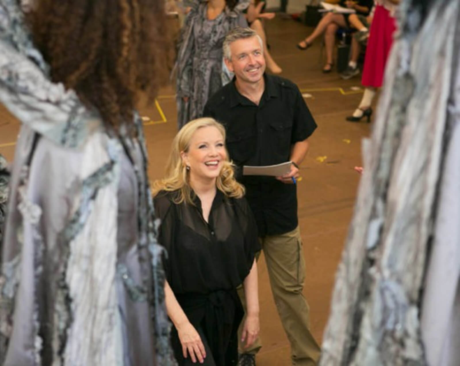Susan Stroman and associate Chris Peterson in rehearsal, they are looking up at the female ensemble that are on stairs.
