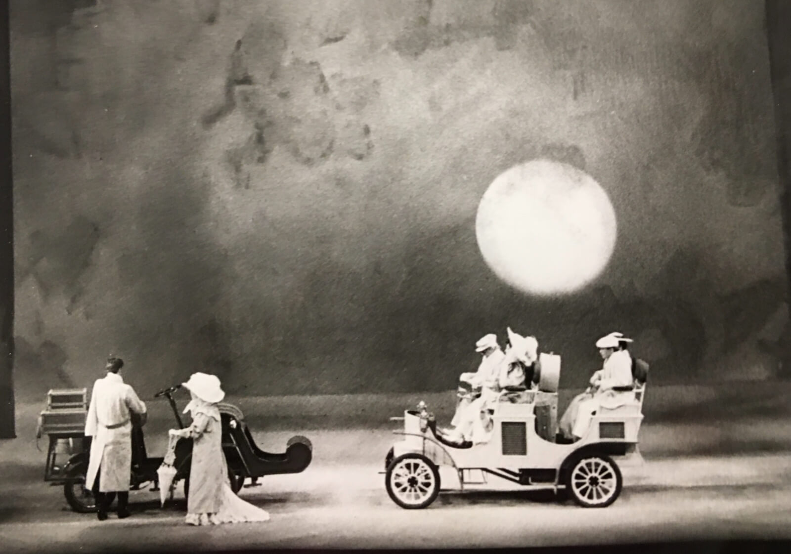 Michael Anania's set for "Night Waltz 2". The sun sits low. There are two couples arriving in cars.
