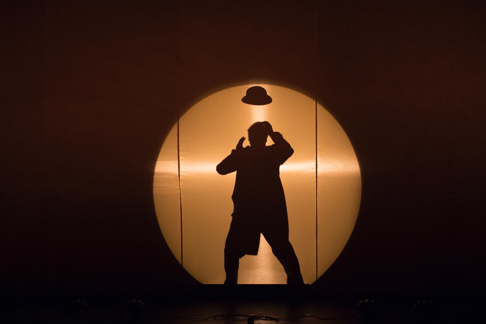 Mandy Patinkin's shadow in a hard edge spot with his hat floating over his head.
