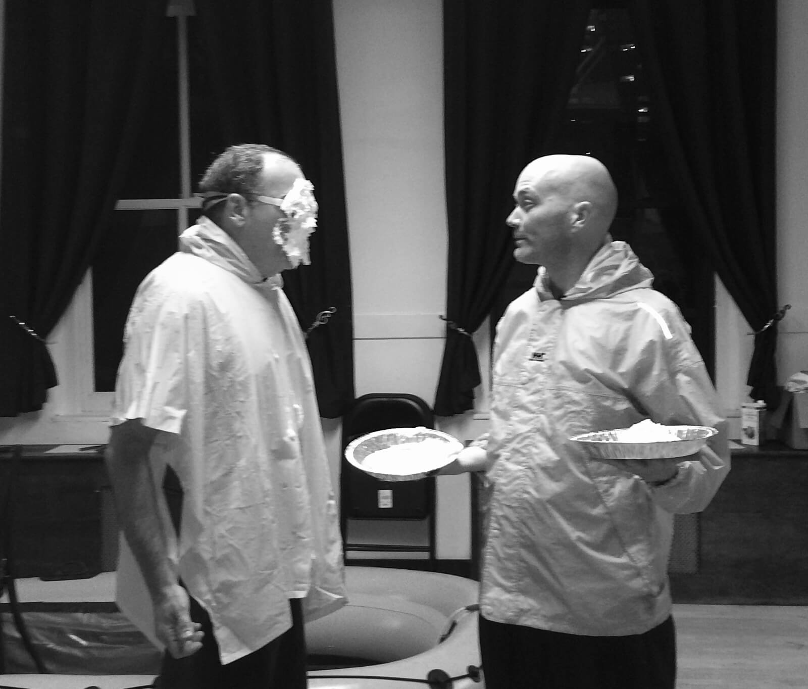 Mandy Patinkin and Taylor Mac rehearsing a scene with pies. Mandy has face covered in whipped cream while Taylor holds the empty pie plate. 