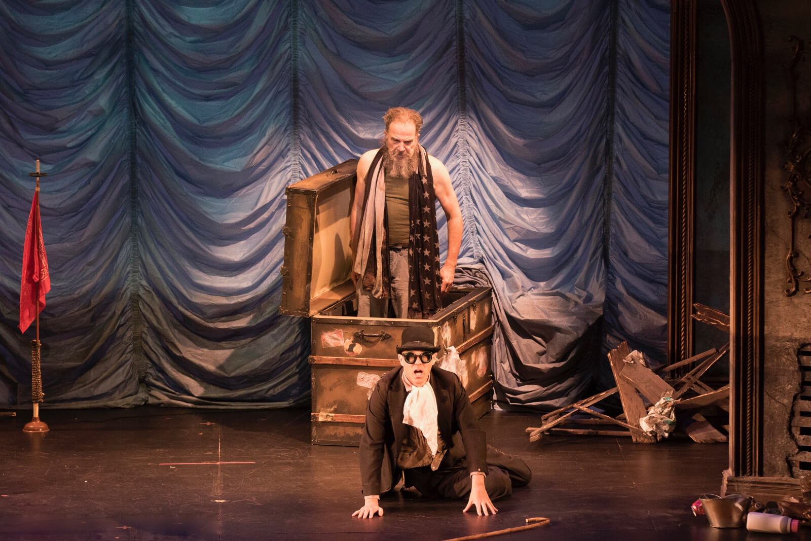 Mandy Patinkin and Taylor Mac in a scene from The Last Two People on Earth: An Apocalyptic Vaudeville. Mandy comes out of a trunk while Taylor sits on the floor, looking terrified.