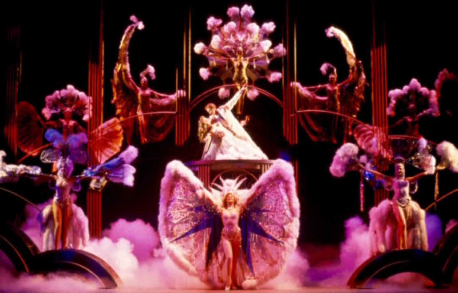 Bobby Child (Harry Groener) gazes at and dips Polly Baker (Jodi Benson) on a platform while surrounded by dancers in elaborate costumes for the Finale