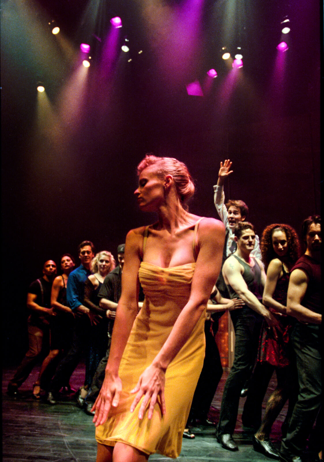 Girl in the Yellow Dress (Deborah Yates) dances downstage center as the club-goers are in a single file line behind her. Boyd Gaines is trying to get her attention as he is behind the line of ensemble members. 