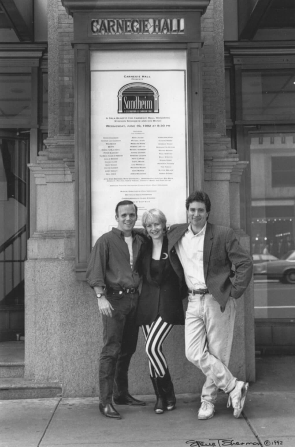 Scott Ellis, Susan Stroman and David Thompson. A black and white photo of the team posing in front of the Sondheim poster at the Carnegie Hall.