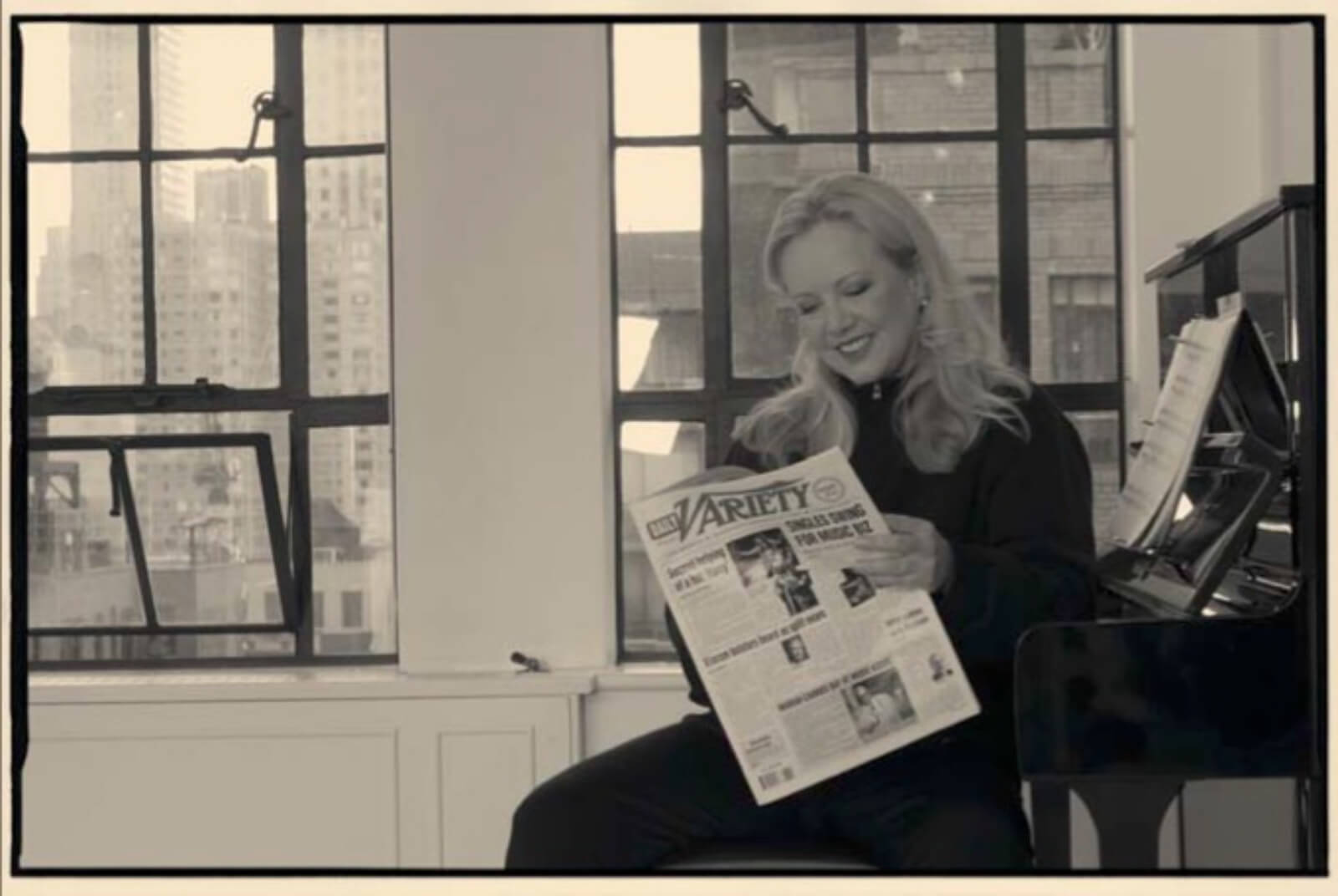 Portrait of Susan Stroman in her studio, sitting on the bench next to her piano, reading Variety.