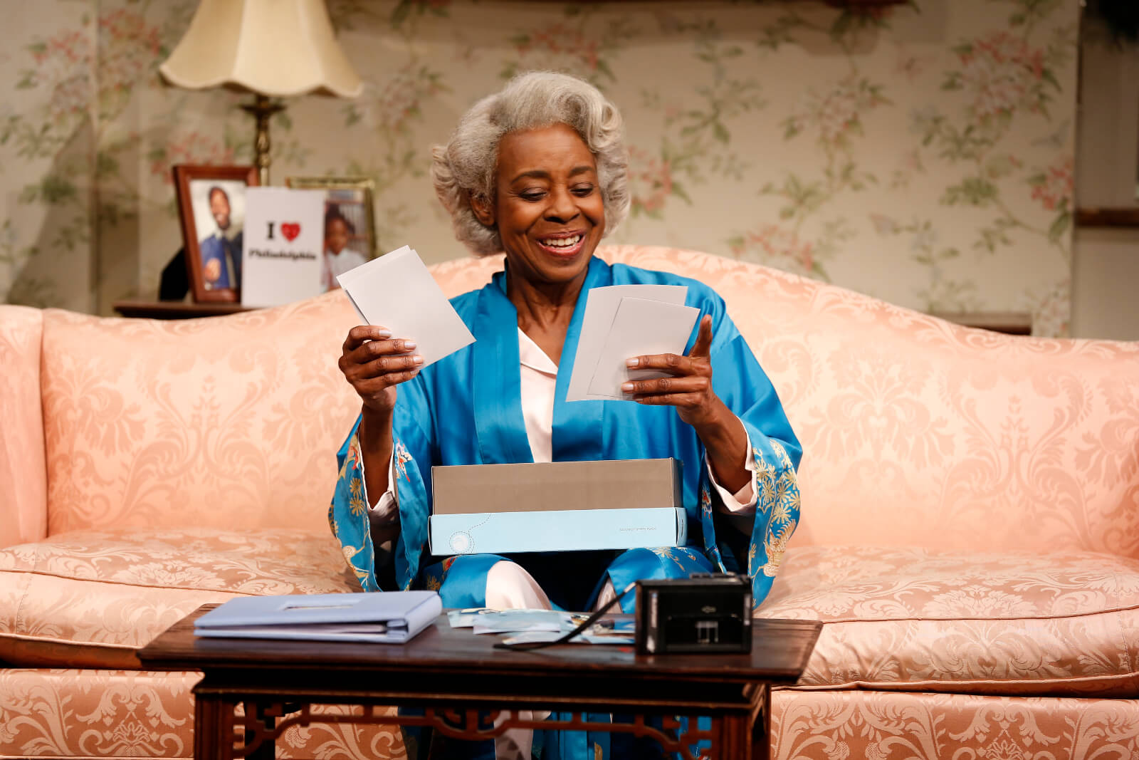 Dotty (Marjorie Johnson) pulls photos out of a shoebox and smiles while sitting on a couch.