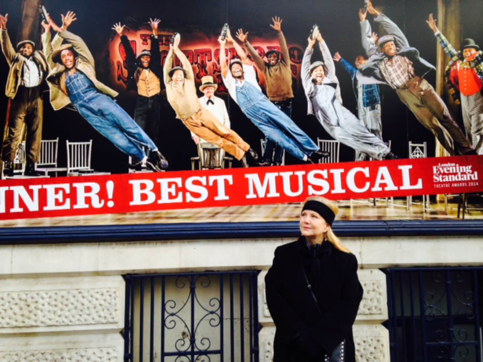 Susan Stroman (in black jacket and headband) outside of The Scottsboro Boys marquee at the Garrick Theater in London. Show photo and "Best Music" can be seen.