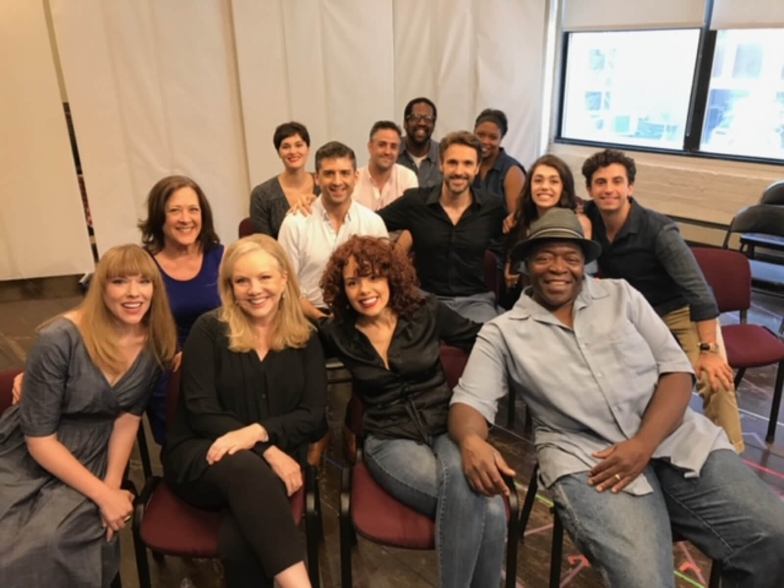 Susan Stroman with the Broadway company of Prince of Broadway. They are in rehearsal sitting in chairs surrounding Susan Stroman. 
