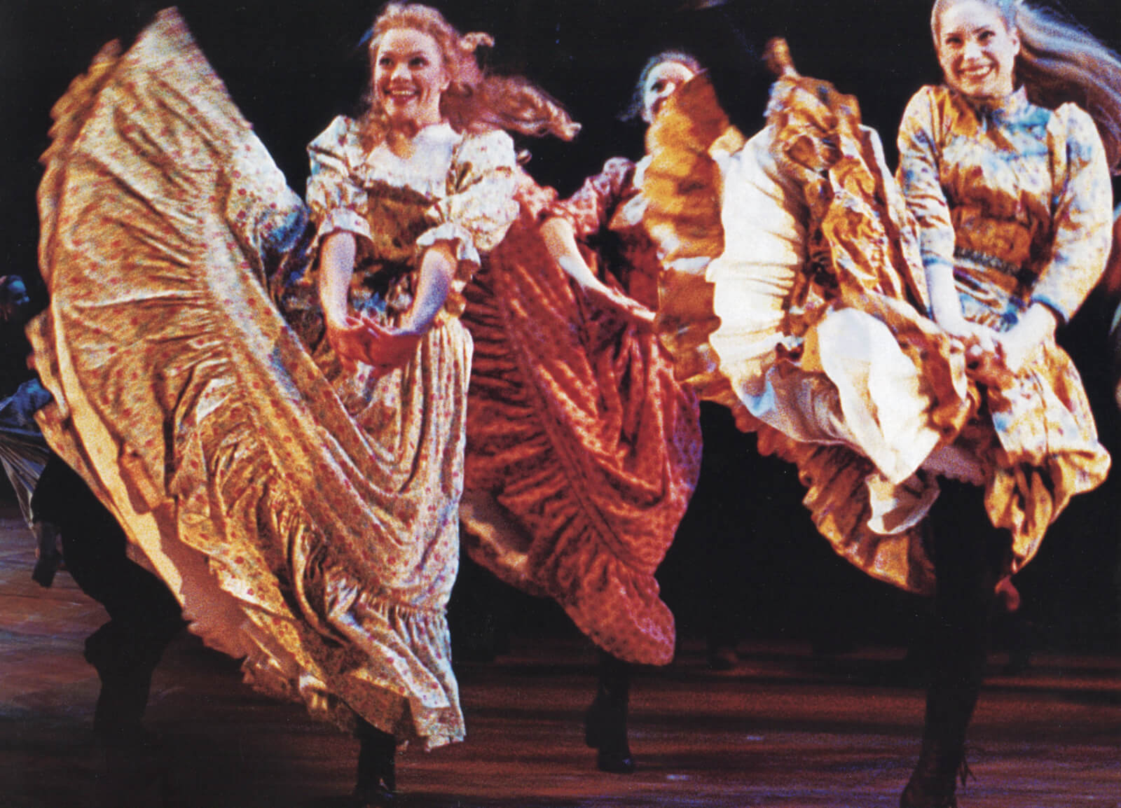 Three ladies in knee-length boots and fluffy dresses kick as high as they could, as part of their dance number.