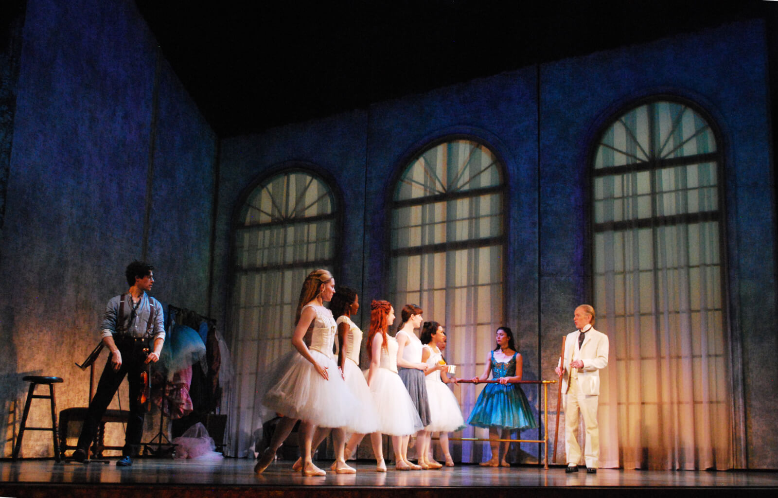 The ballet class from the musical Little Dancer. Ballet dancers dressed in white are listening to their ballet master. A young violinist looks on. 