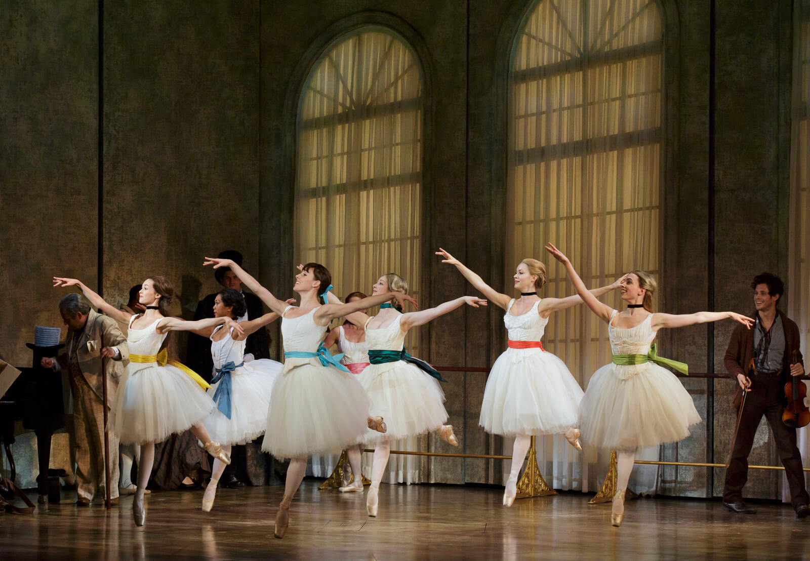 Marie and other ballerinas wearing white ballet outfits with matching colorful hair and belt bows, practicing in a ballet studio with huge windows. A man holding his violin is looking very happy at the back.