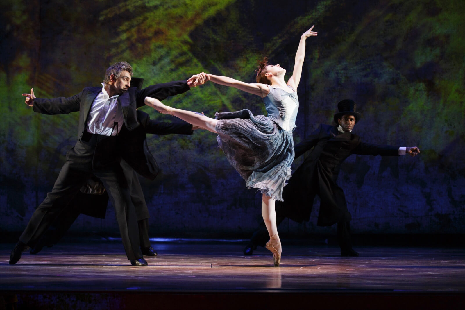 Marie in a powder blue ballet dress and beige shoes, doing a show-stopping arabesque with a partner in a suit.