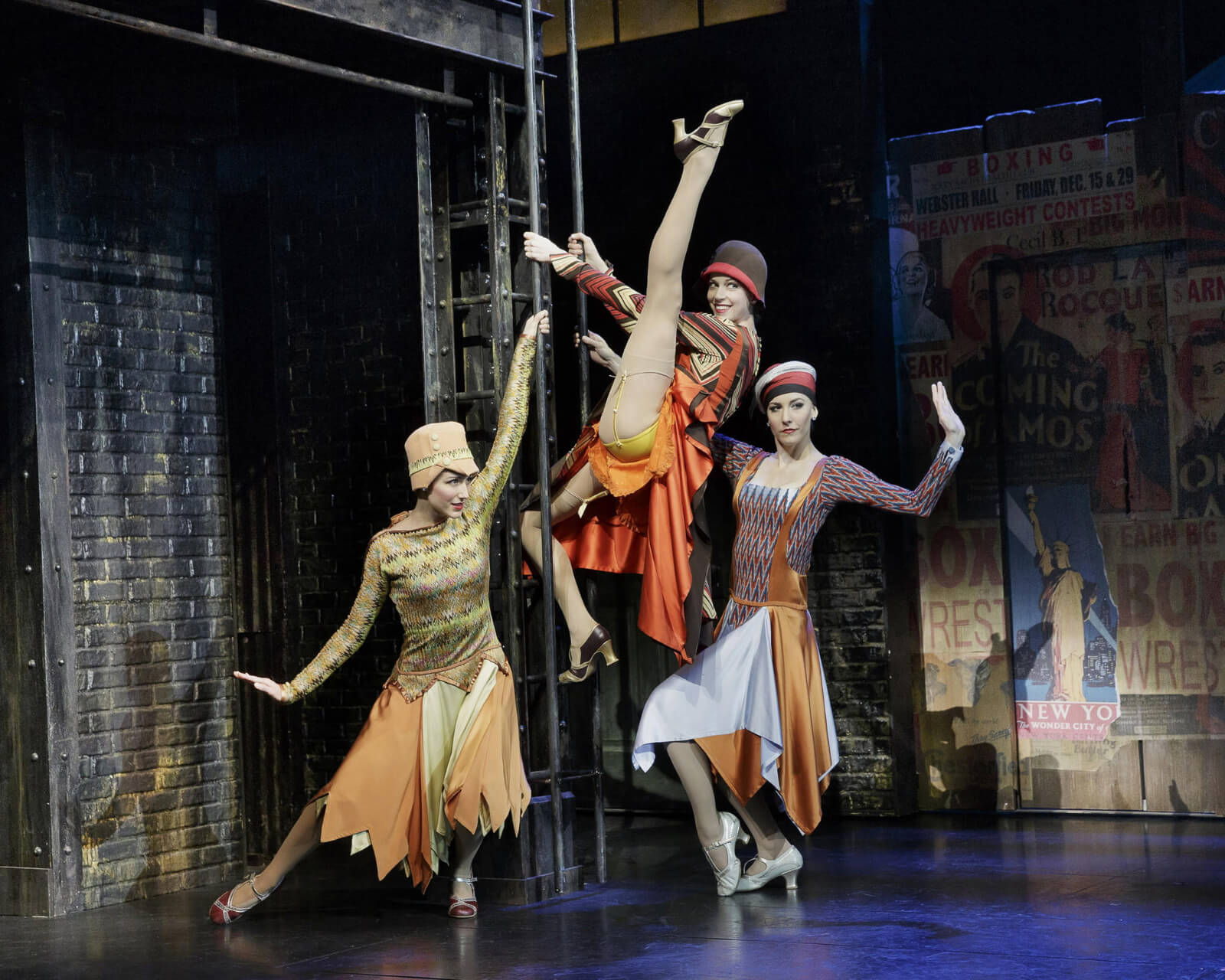3 women in period flapper costumes dancing on a ladder. One has climbed the ladder and is in an extended battement.