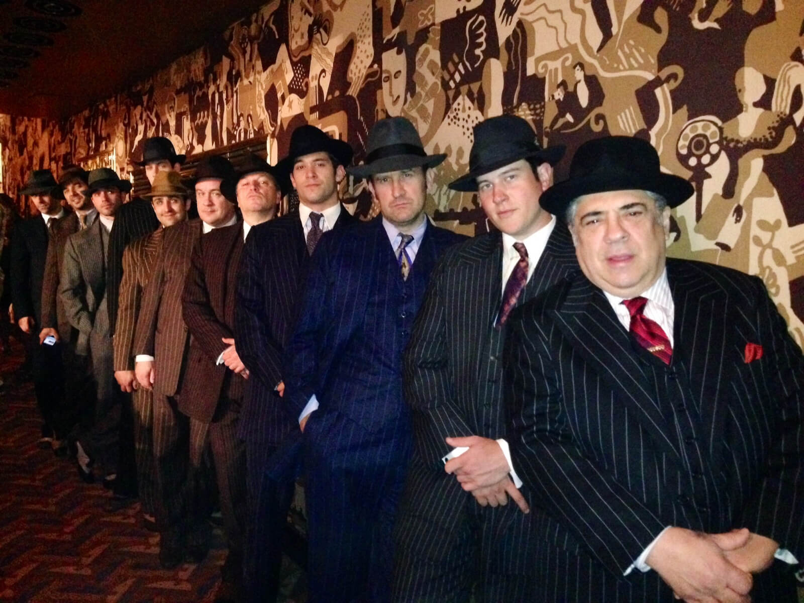 A row of 11 gangsters in pinstripe suits and hats lined up against a wall at Radio City Music Hall.
