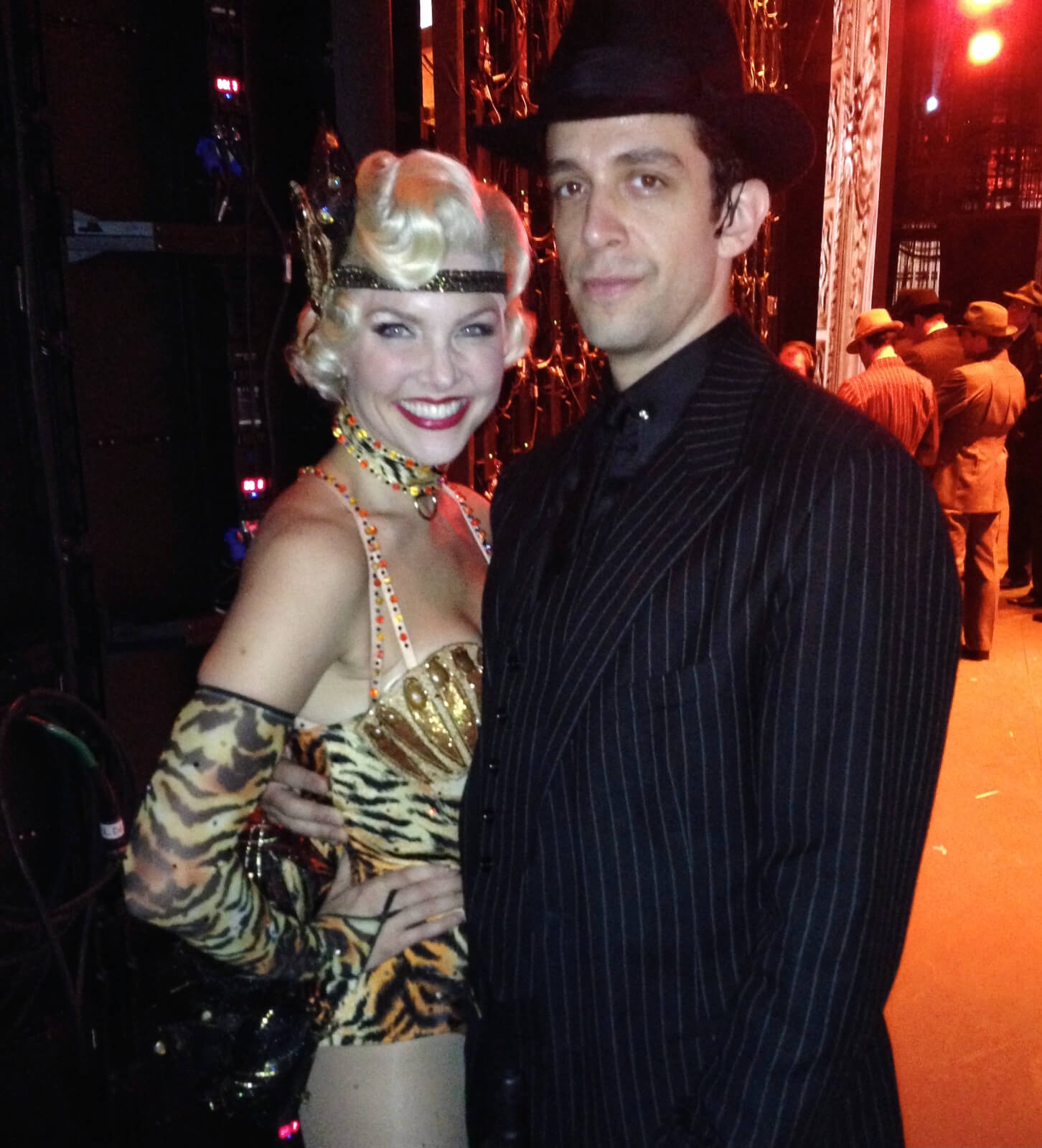 Amanda Kloots in a showgirl outfit and Nick Cordero in a black suit standing backstage in the wing.
