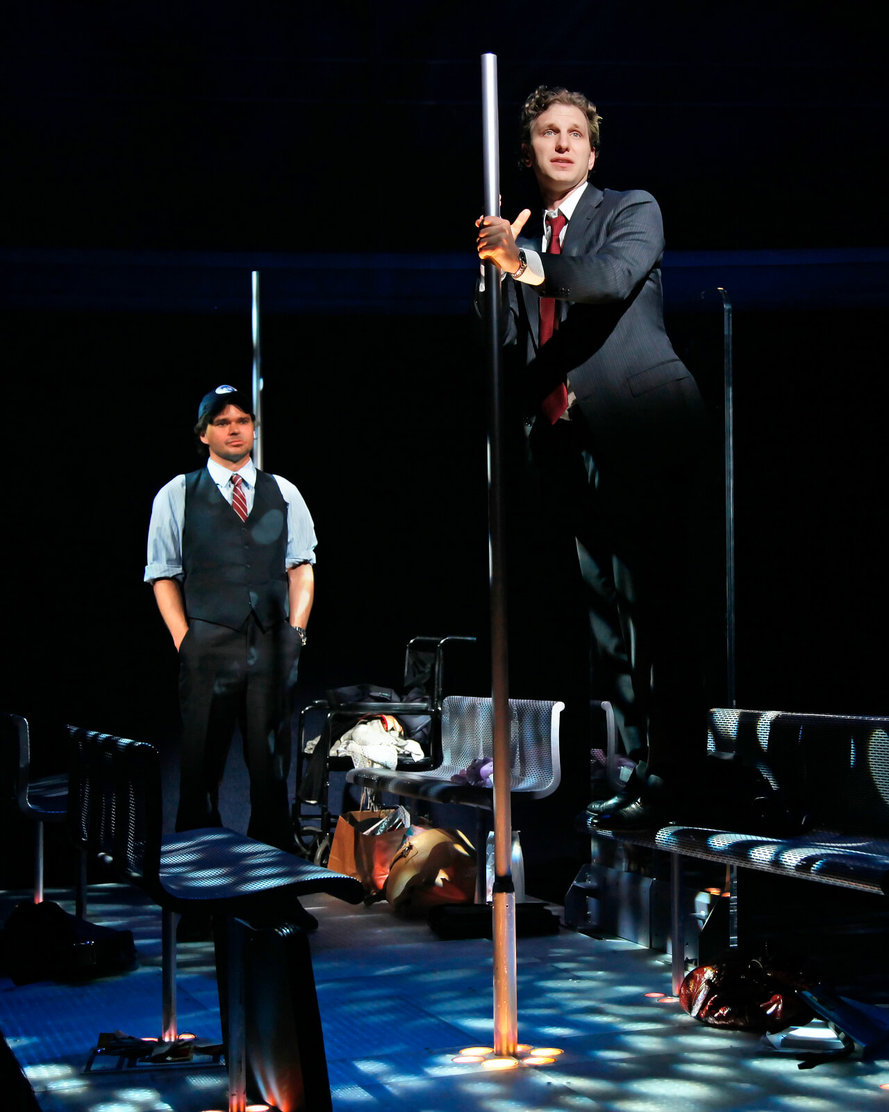 Stanley (Hunter Foster) in an MTA conductor costume looking at Zack (Sebastian Arcelus) in a suit standing on a bench