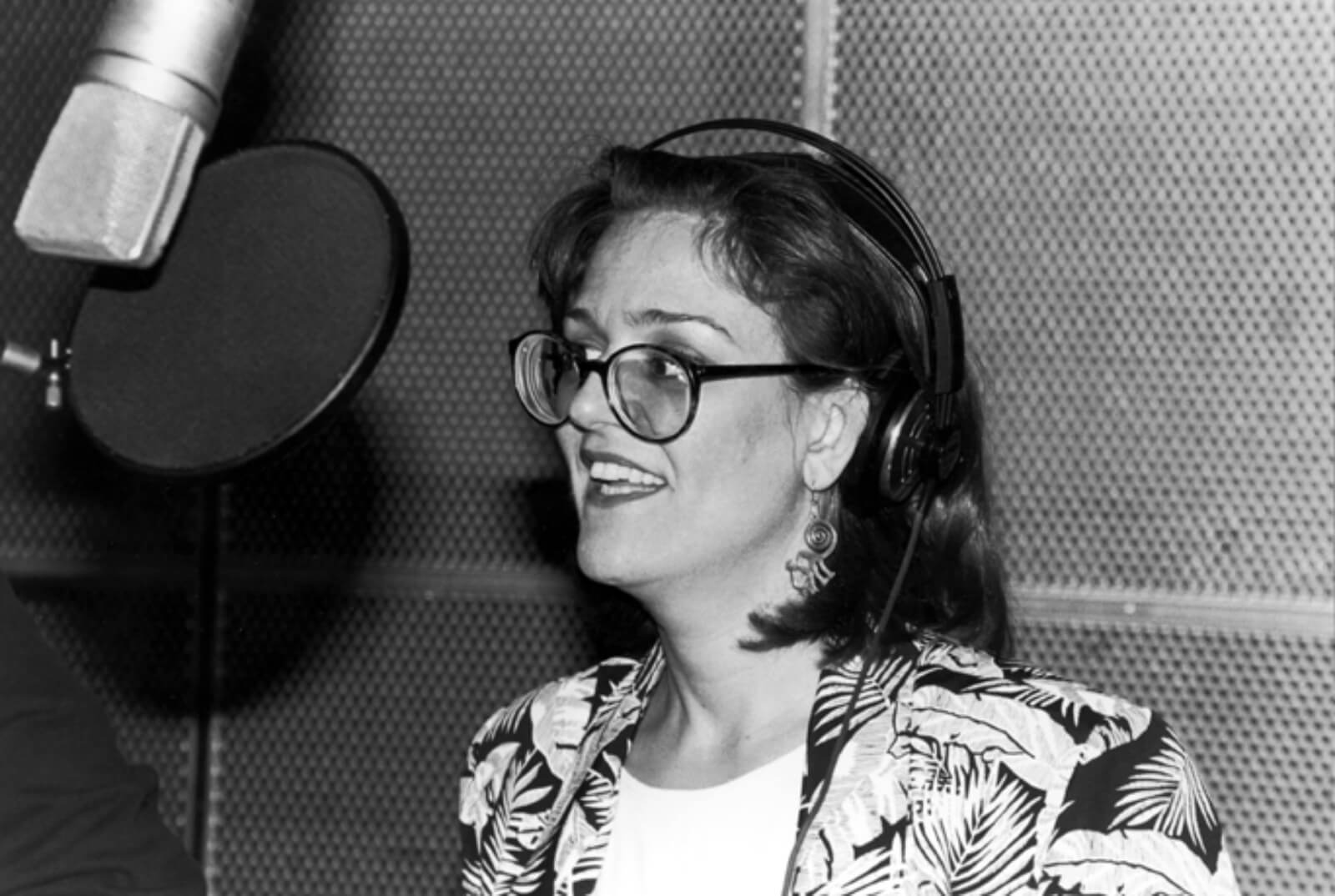 Black and white photo of Karen Mason recording the cast album to And the World Goes ‘Round. She is wearing glasses and a blazer, standing in front of a microphone.