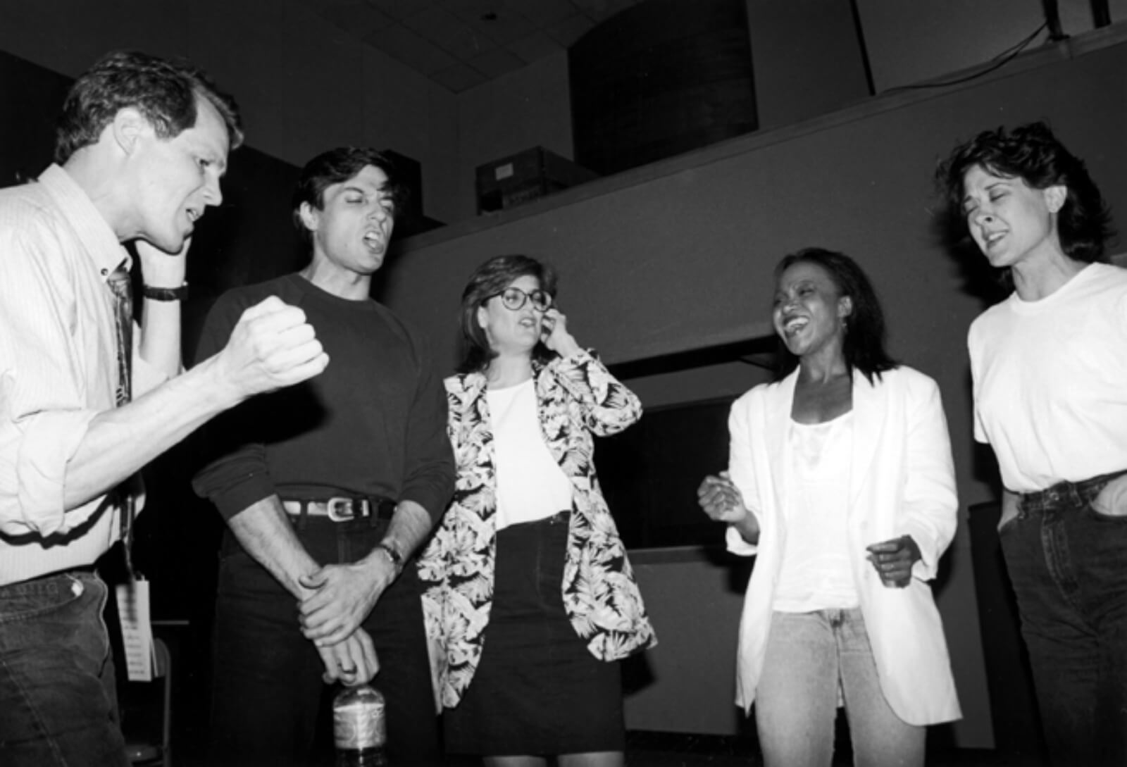 Black and white photo of Jim Walton, Bob Cuccioli, Karen Mason, Brenda Pressley and Karen Ziemba recording "Cabaret". They are standing in a circle: some with one hand to their ear or eyes closed.