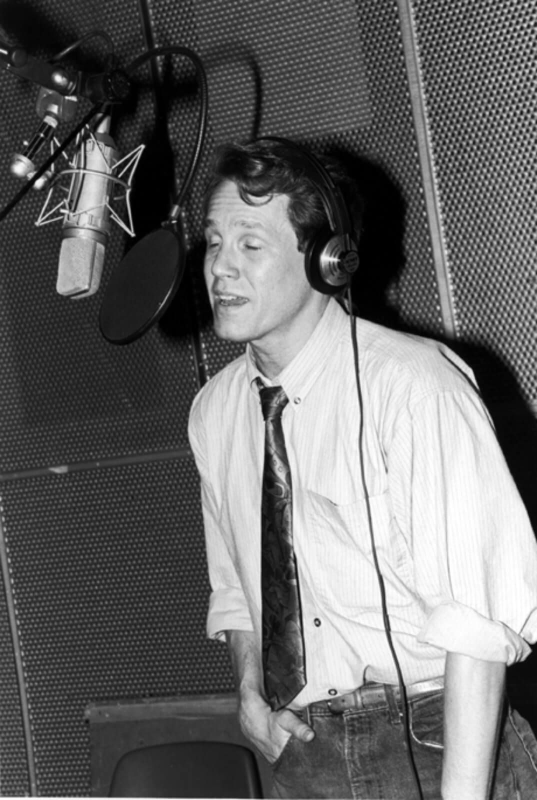 Black and white photo of Jimmy Walton recording the cast album to And the World Goes ‘Round. He is standing in front of a microphone and wearing a tie.
