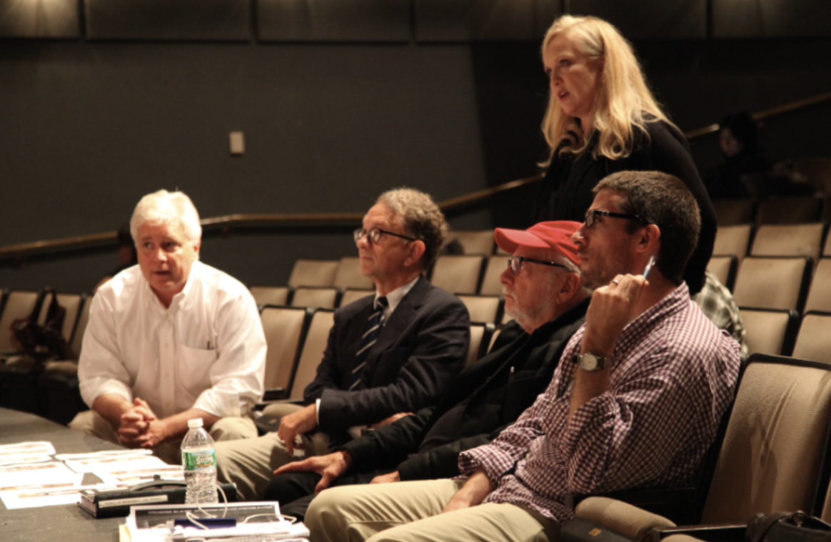 The show's creatives in rehearsal, four of them sitting in the front seats of an empty theatre. Susan Stroman is directing the cast on stage.