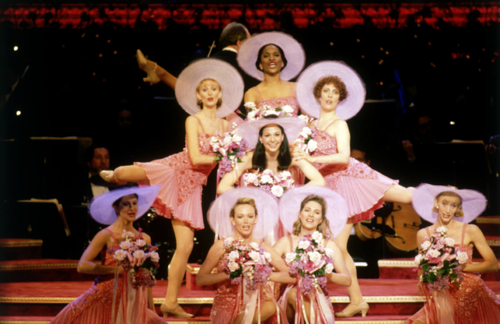 The “Getting Married Today” Ensemble: wearing pink frilly dresses, holding flowers, and in a tableau.