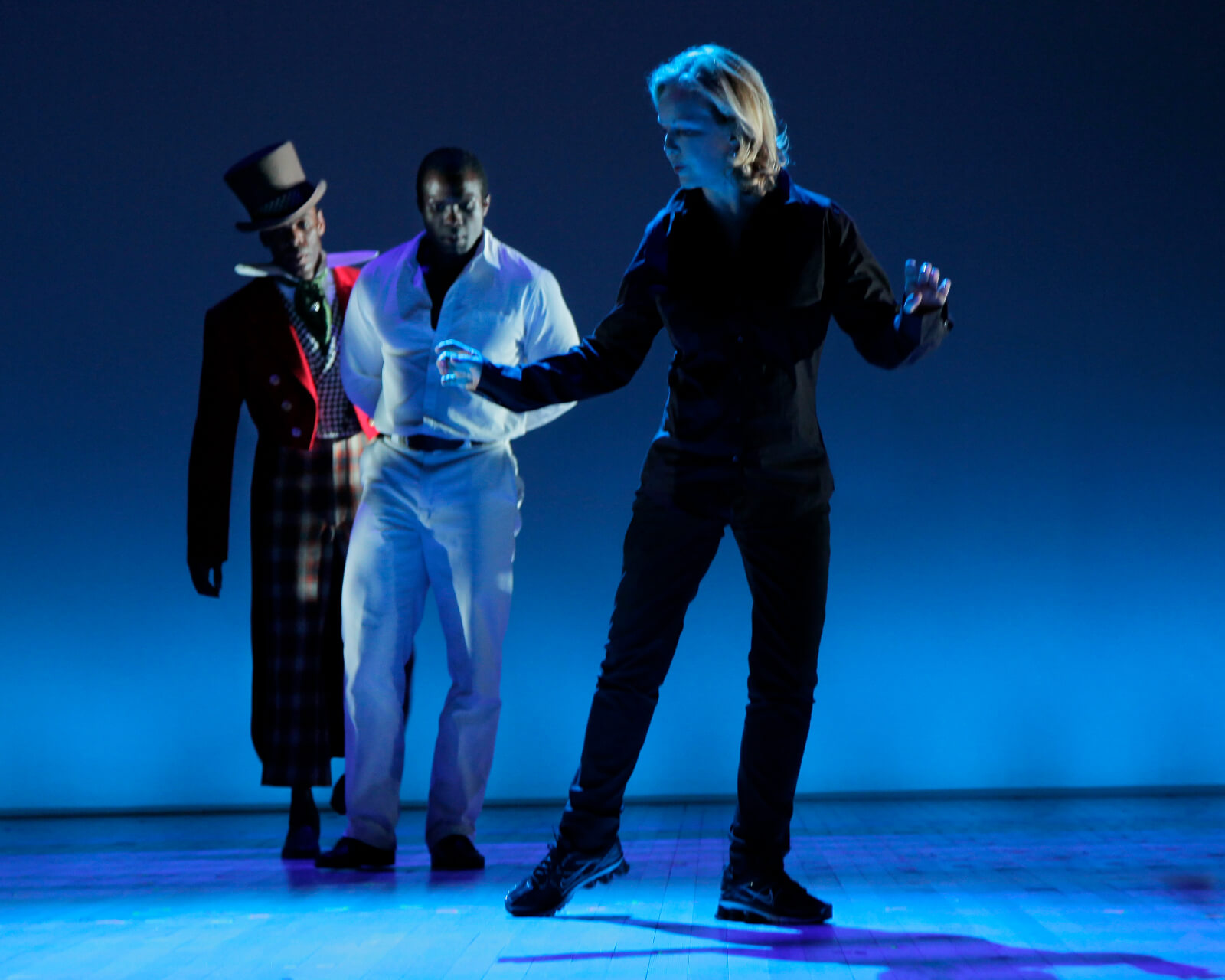 Stro onstage in blue lighting rehearsing The Scottsboro Boys with two actors in costume upstage watching.