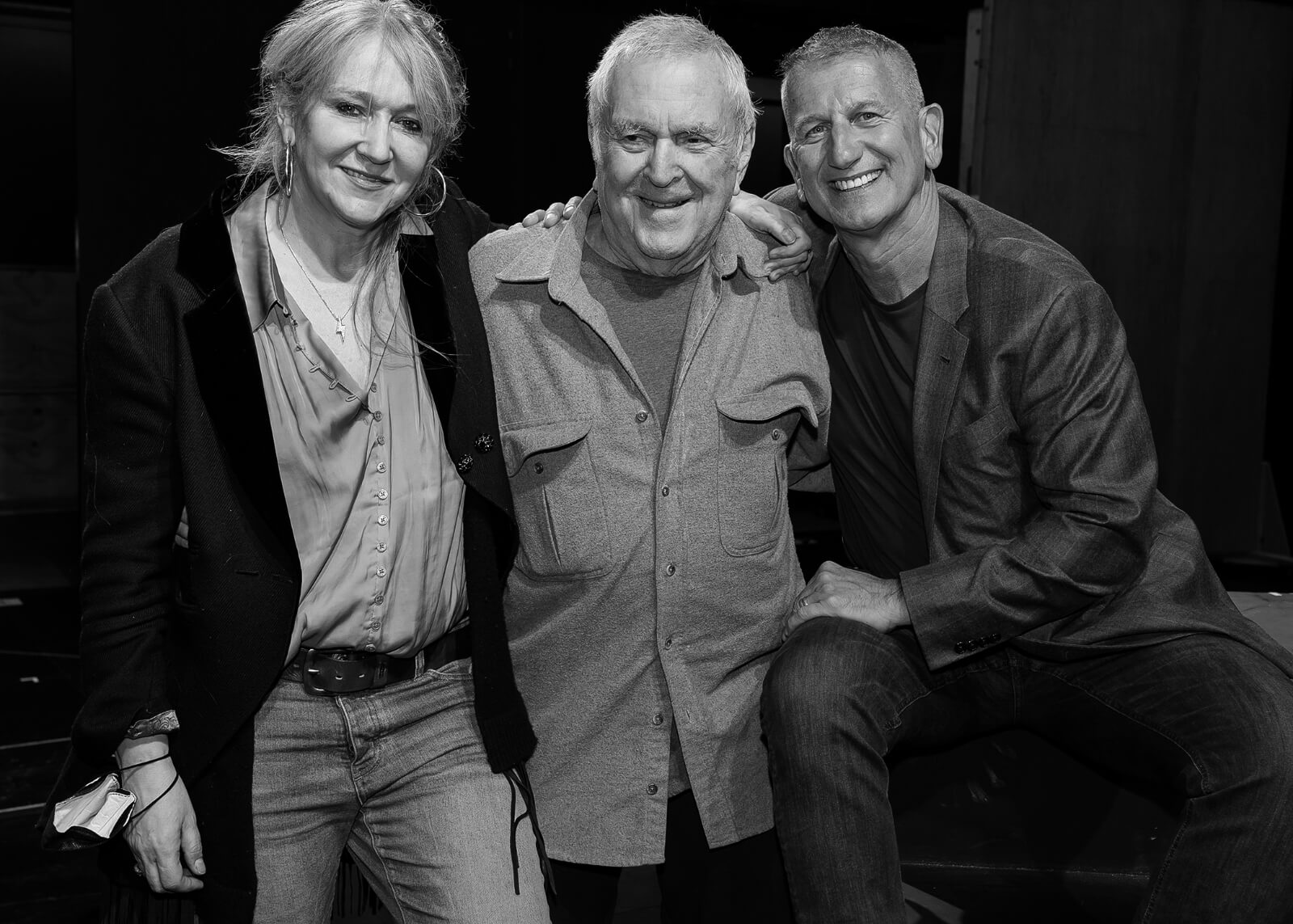 Black and white photo of Producer Sonia Friedman, Composer John Kander and Producer Tom Kirdahy with arms around one another.