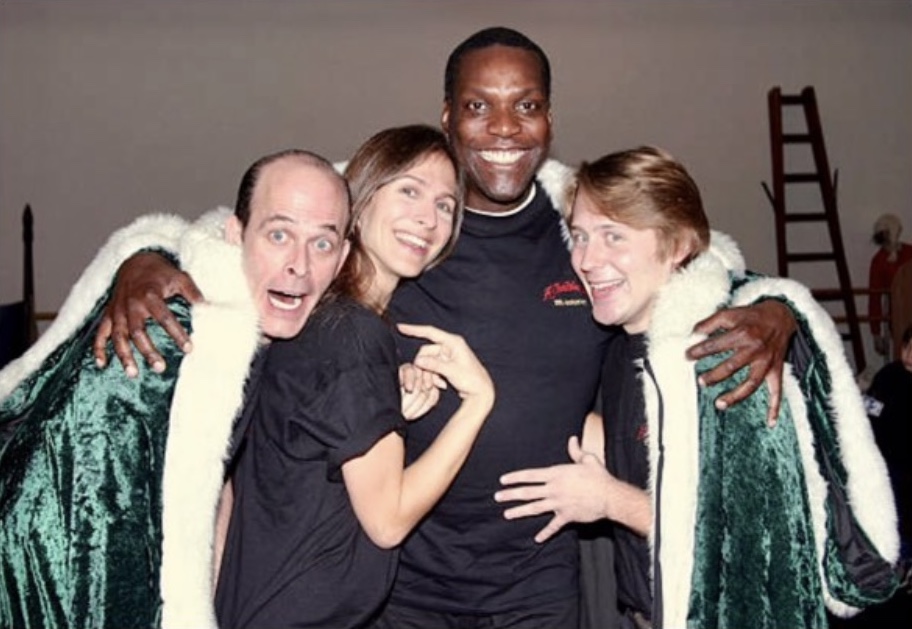 Paul Kandel (Marley), Catherine Batcheller (Ghost of Christmas Future), Gerry McIntyre (Ghost of Christmas Present), and Justin Brill (Ghost of Christmas Past) rehearsing at Madison Square Garden. They are dressed in black but covered in green holiday robes lined with white fur.