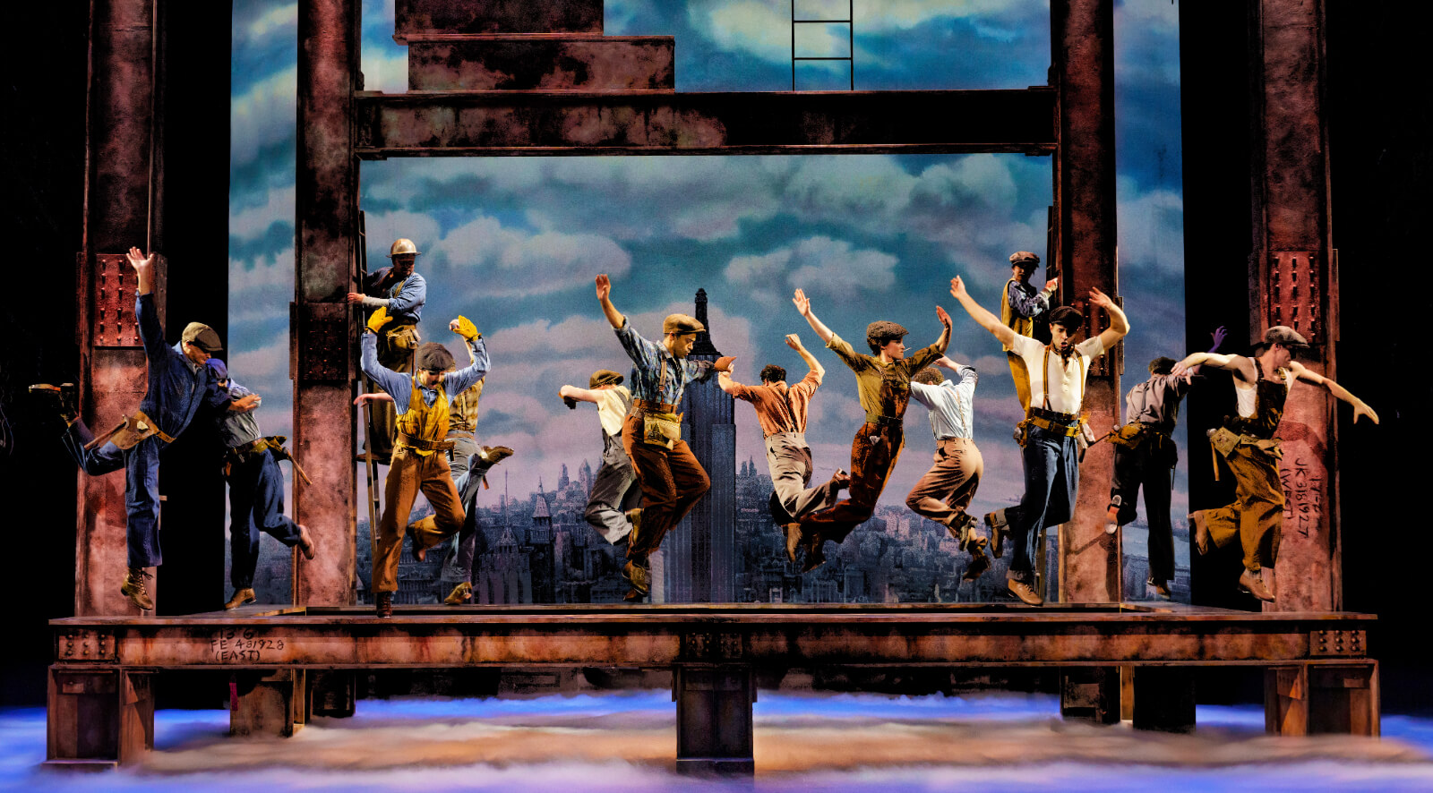The cast of New York, New York performing in “Wine and Peaches.” Dancers are scene dancing on high beams with clouds below them and the sky behind them.