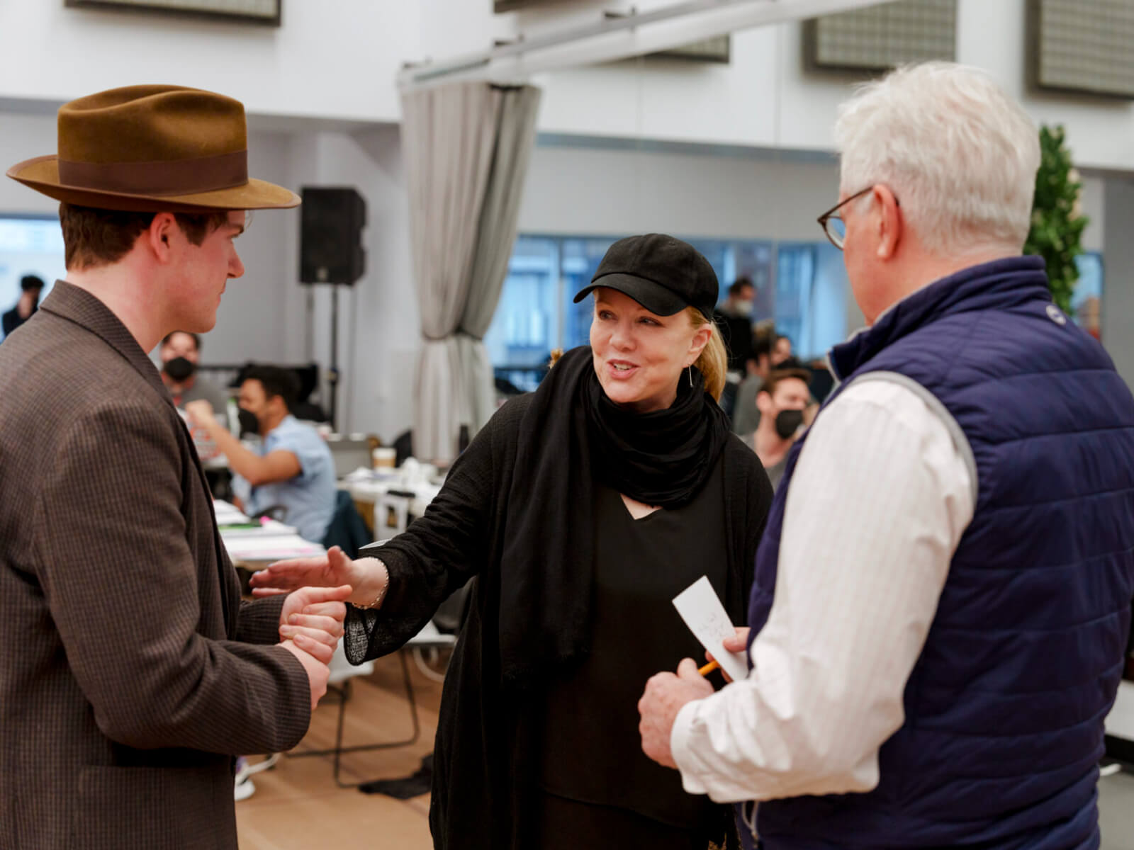 Colton Ryan, Susan Stroman and David Thompson in rehearsal for New York, New York. Colton is wearing a rehearsal hat and blazer, David holds a note card, and Stro is wearing signature rehearsal blacks and hat - standing between the men and speaking to Colton.