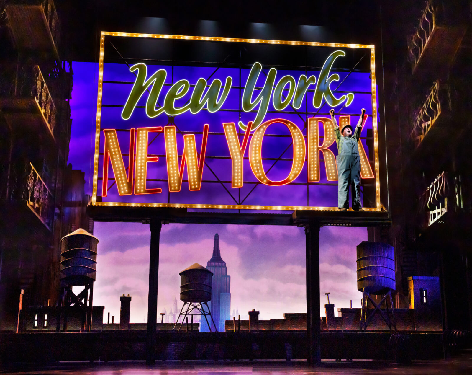 Opening scene in New York, New York with Jim Borstelmann. He stands in front of a neon billboard sign saying "New York, New York" with both hands raised while shouting "I love this city!"