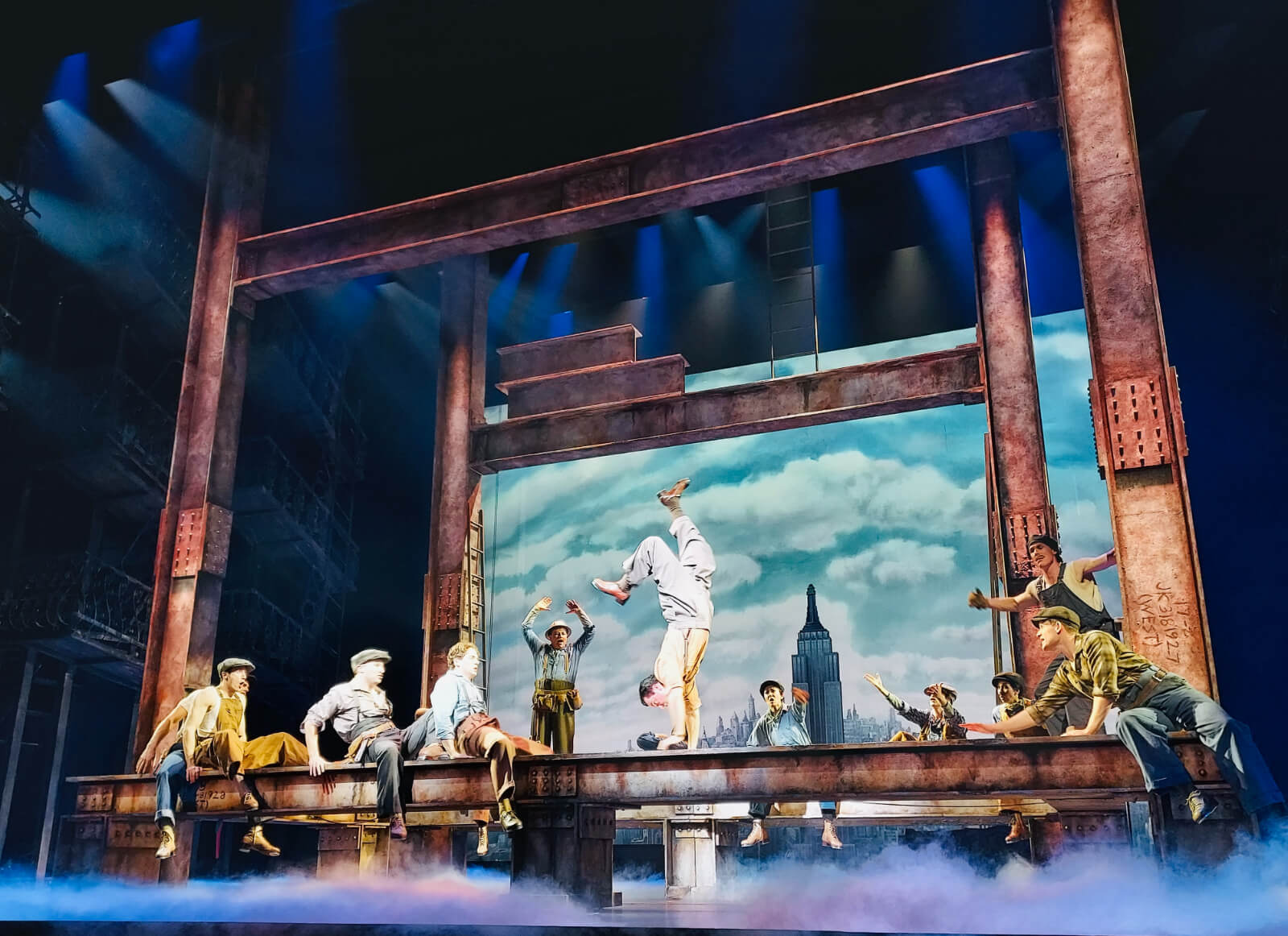 Moment from “Wine and Peaches.” Male dancer is doing a handstand walk across a metal beam while other male dancers cheer them on.