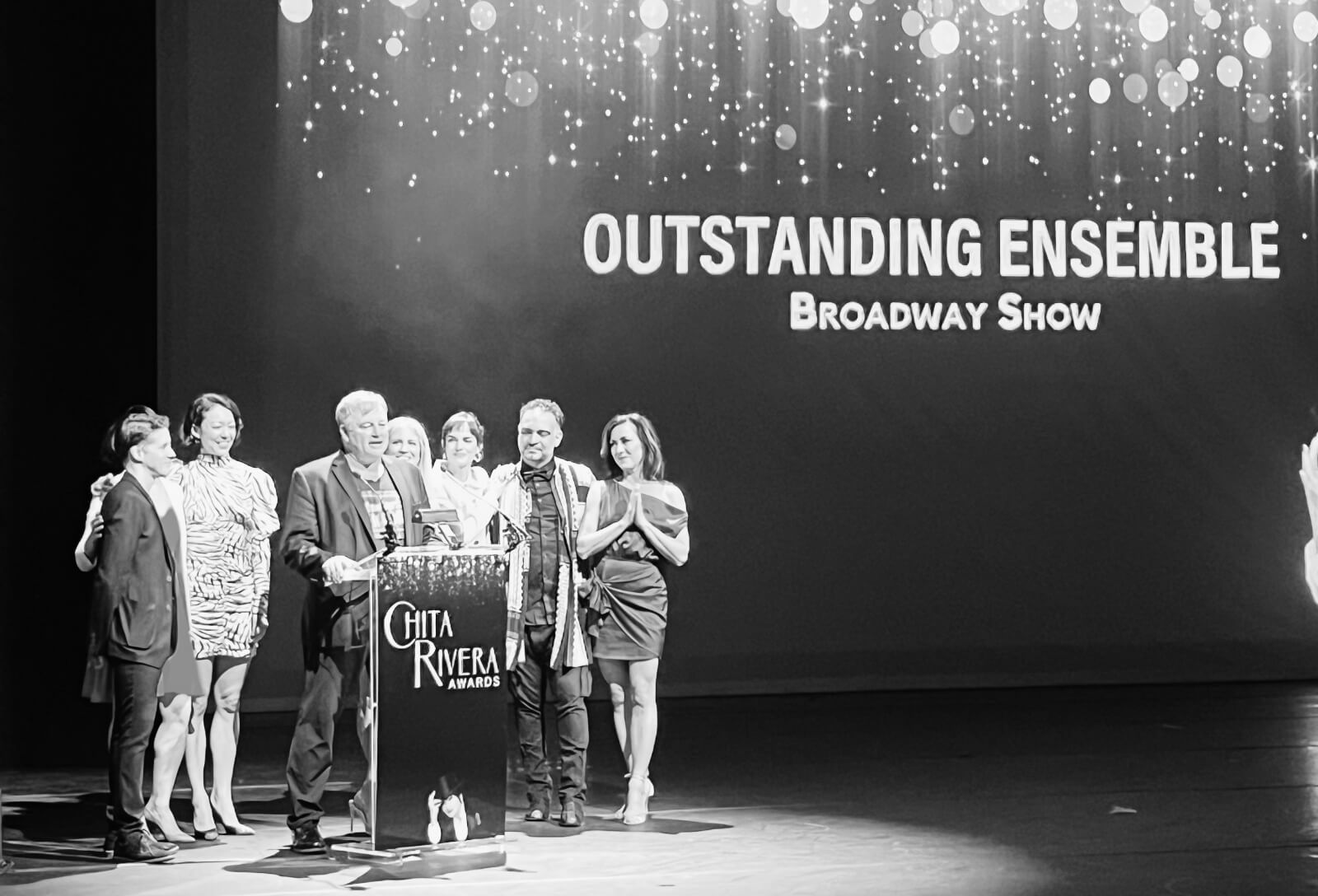 Black and white photo showing the Ensemble of New York, New York accepting the Chita Rivera Award for Outstanding Ensemble on Broadway at the awards ceremony.