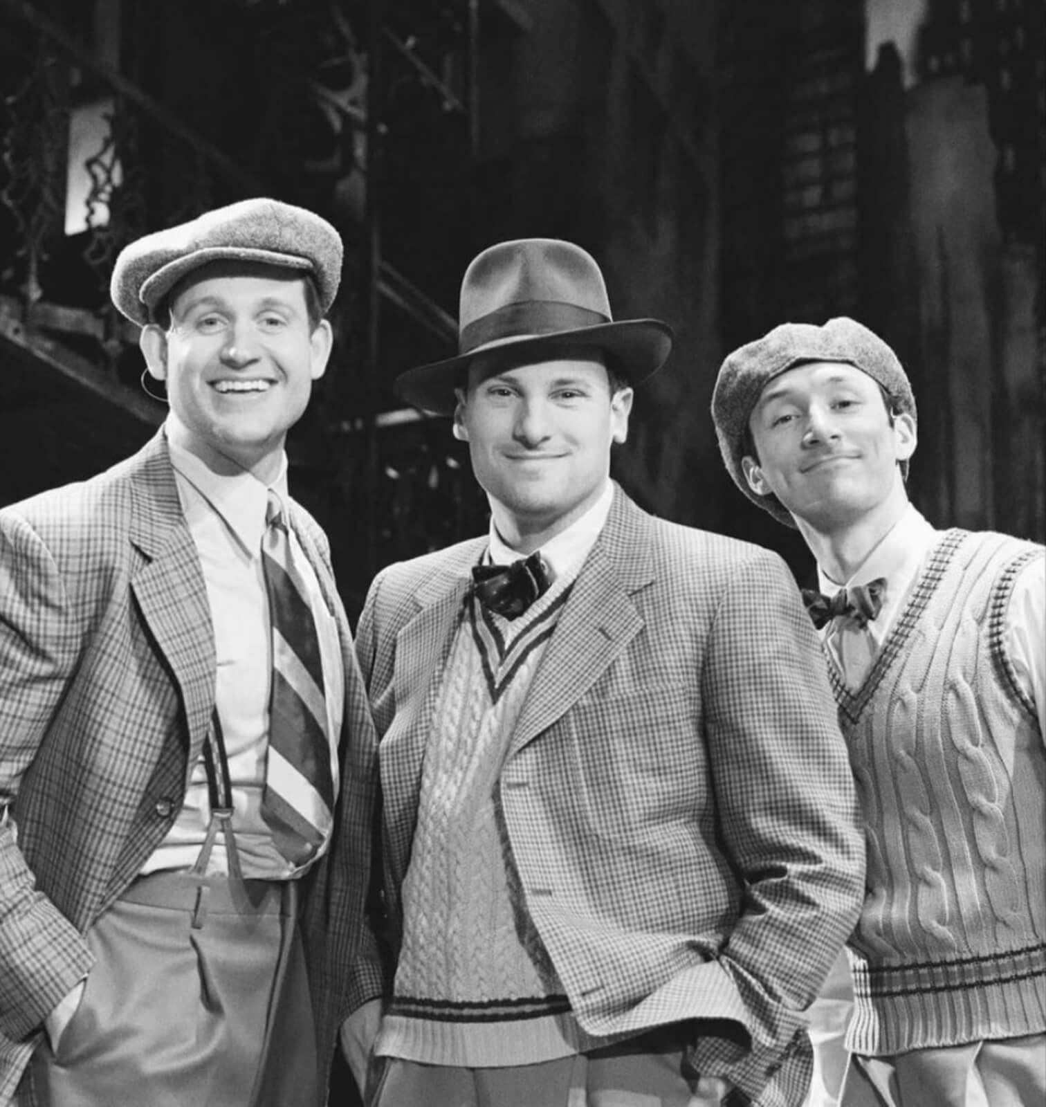 Black and white photo of Giovanni Bonaventura, Richard Gatta, Drew Redington backstage at New York, New York. They are wearing variations of 3 piece suits and hats from the 50s: think wool and tweed fabrics.