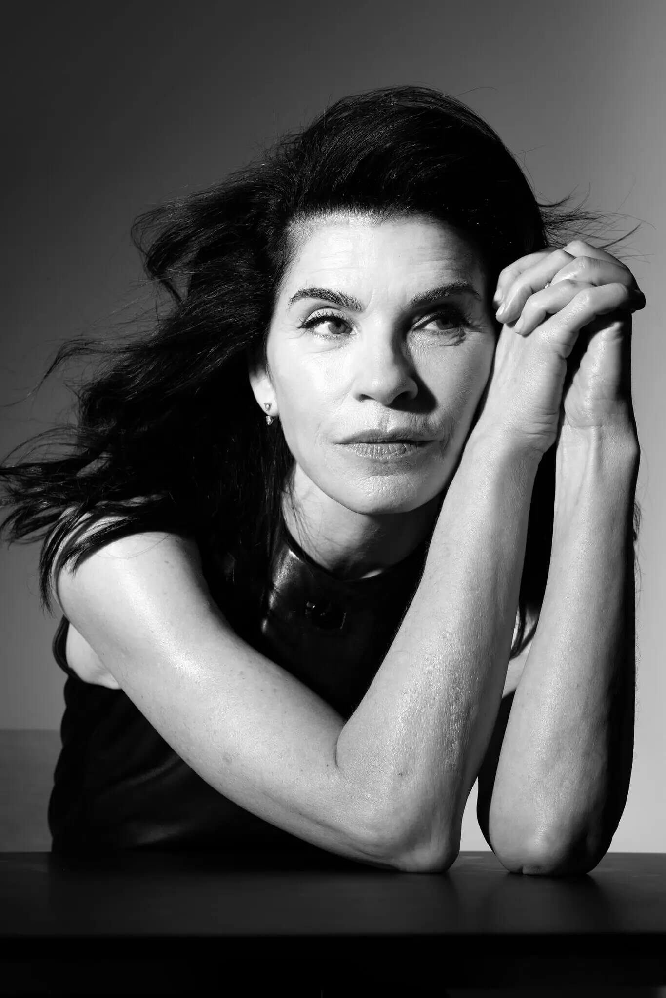 Black and white photo of Julianna Margulies with head beside her two clasped hands.