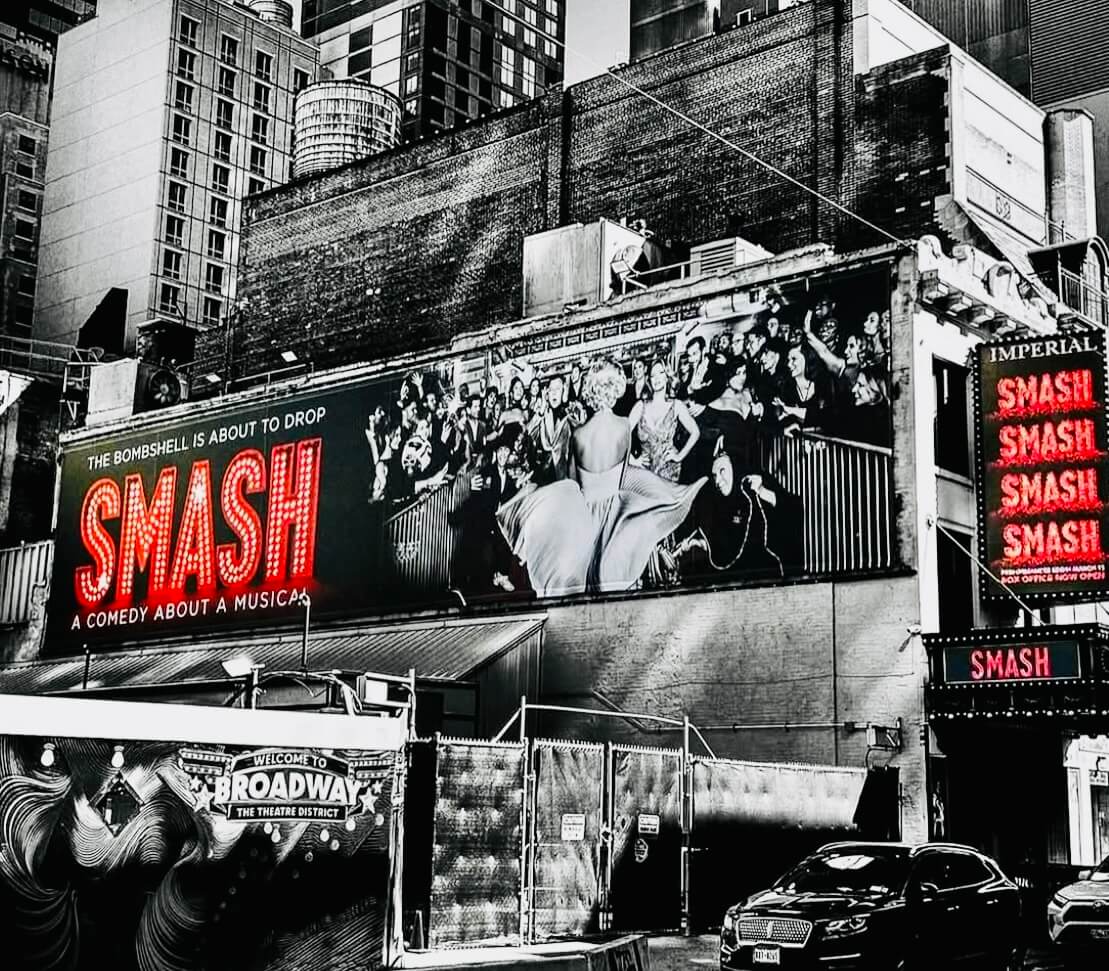 The exterior of the Imperial Theatre in New York City featuring bold red signage for SMASH and a large billboard with a Marilyn Monroe figure facing a cheering crowd.