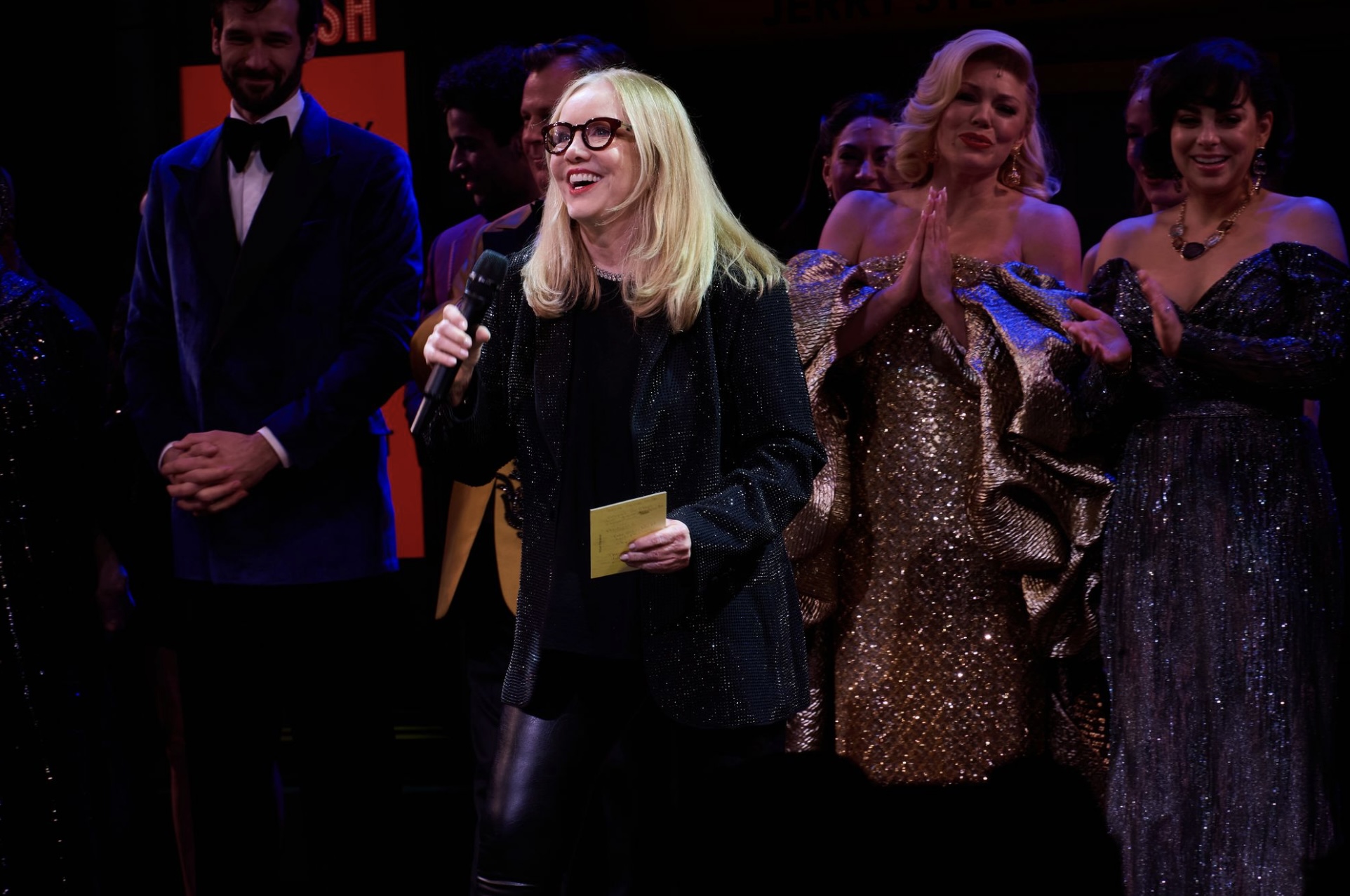 Susan Stroman speaks on stage at the Imperial Theatre during SMASH's opening night, surrounded by cast members in glamorous costumes.