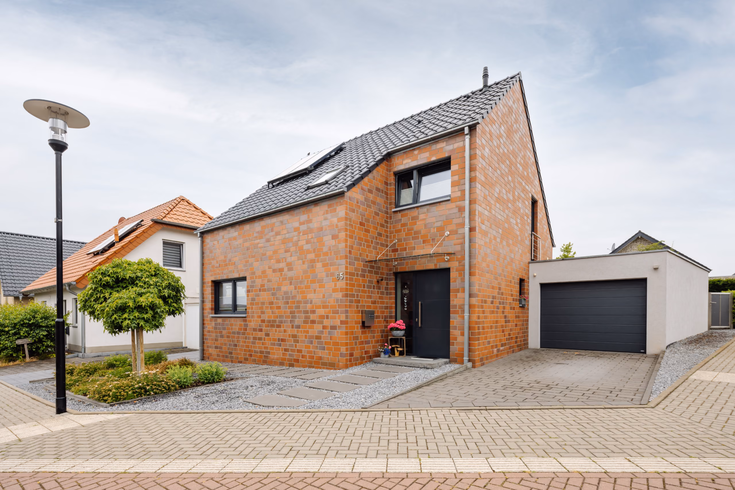 Modernes zweistöckiges Haus mit roter Backsteinfassade, schwarzem Eingang und angrenzender Garage.