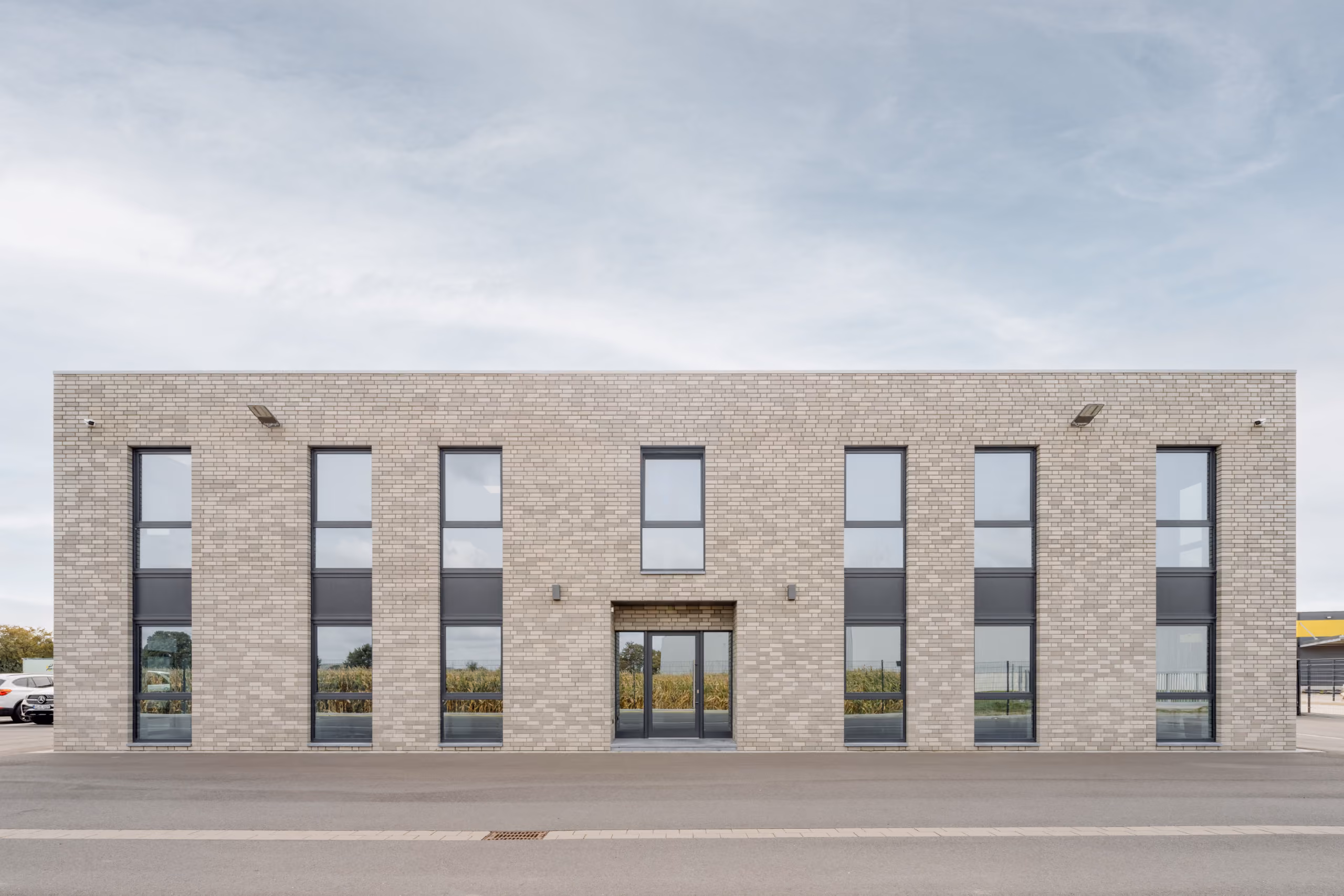 Moderne zweistöckige Fassade aus hellen Ziegeln mit großen Fensterfronten und Doppeltür im Zentrum.