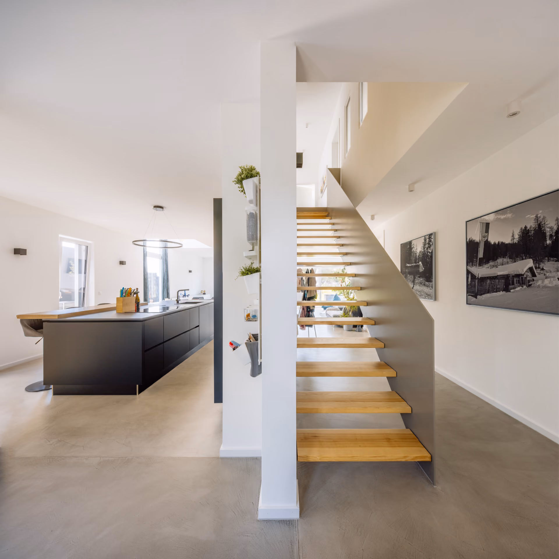 Moderner Innenraum mit Holztreppe, schwarzen Küchenmöbeln und minimalistischer Einrichtung.
