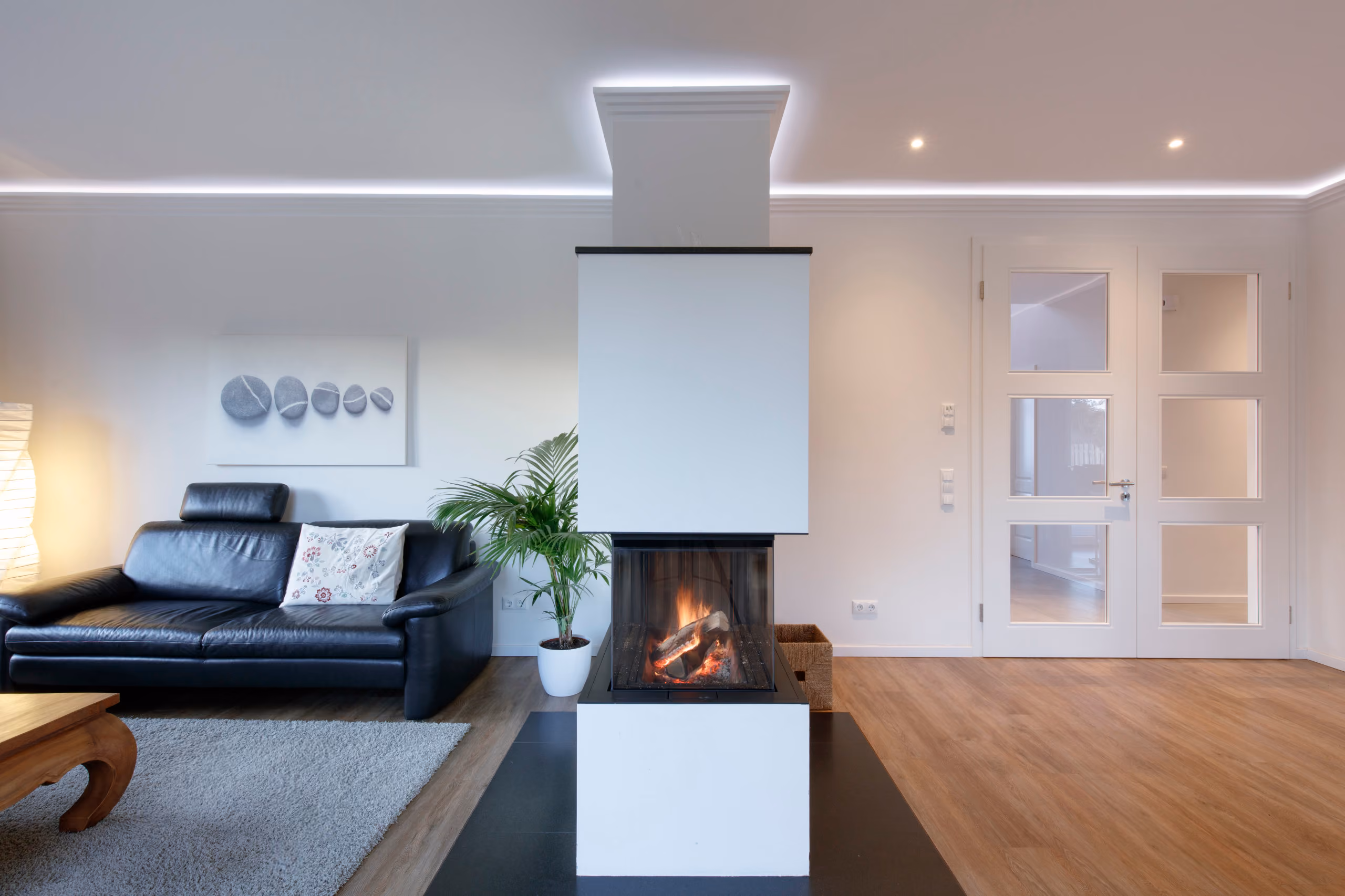 Moderner Wohnraum mit Kamin in der Mitte, schwarzem Ledersofa, grauem Teppich und Holzboden.