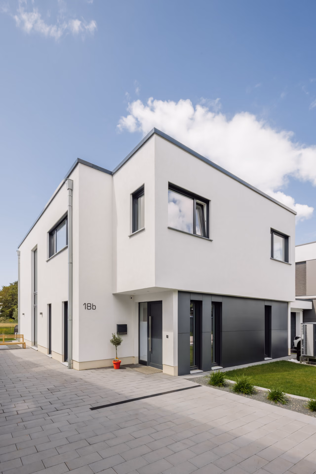 Modernes weißes zweistöckiges Wohnhaus mit großen Fenstern und grauen Akzenten unter blauem Himmel.