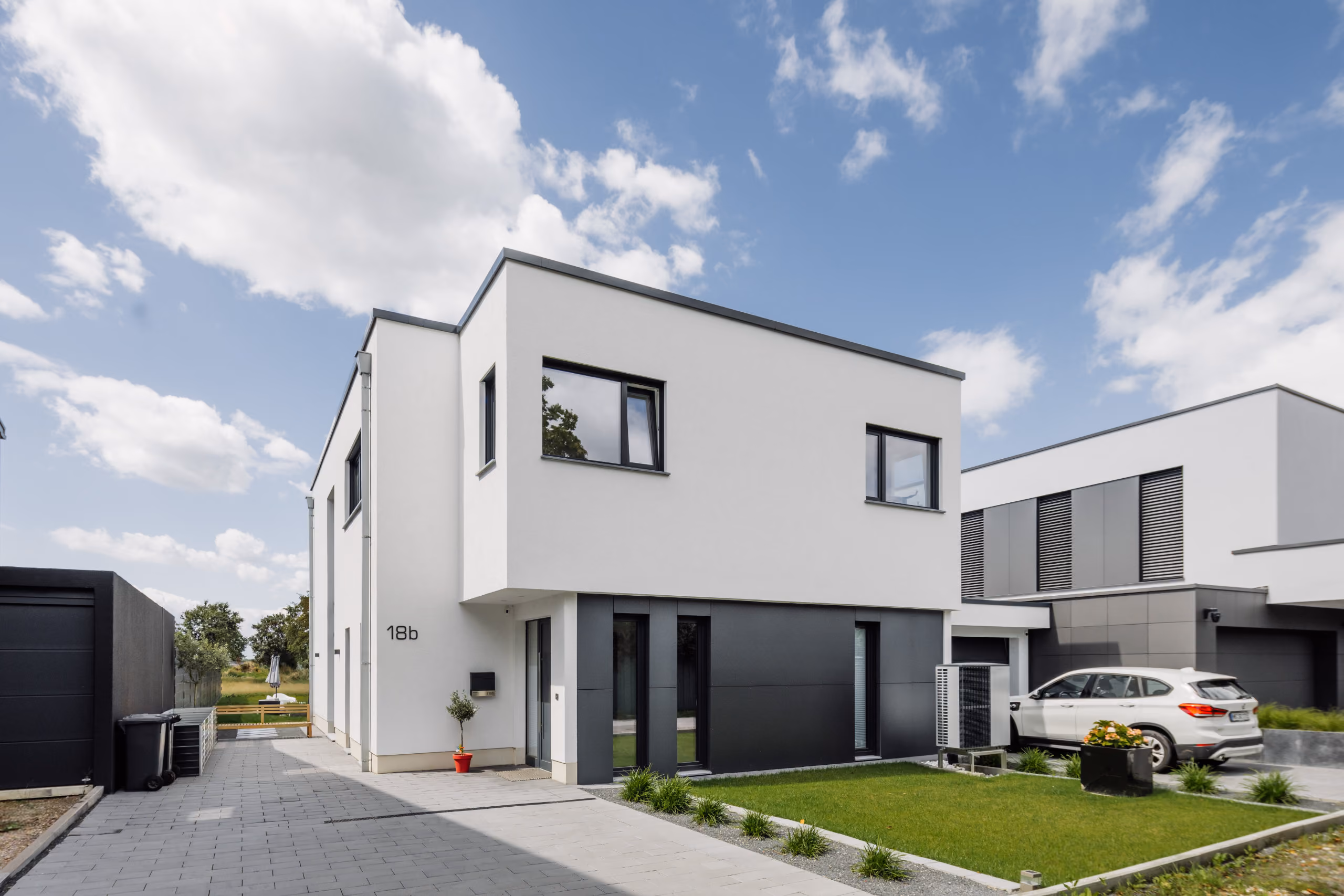 Modernes zweistöckiges Haus mit weißer Fassade, schwarzer Tür, Grasfläche und geparktem Auto.