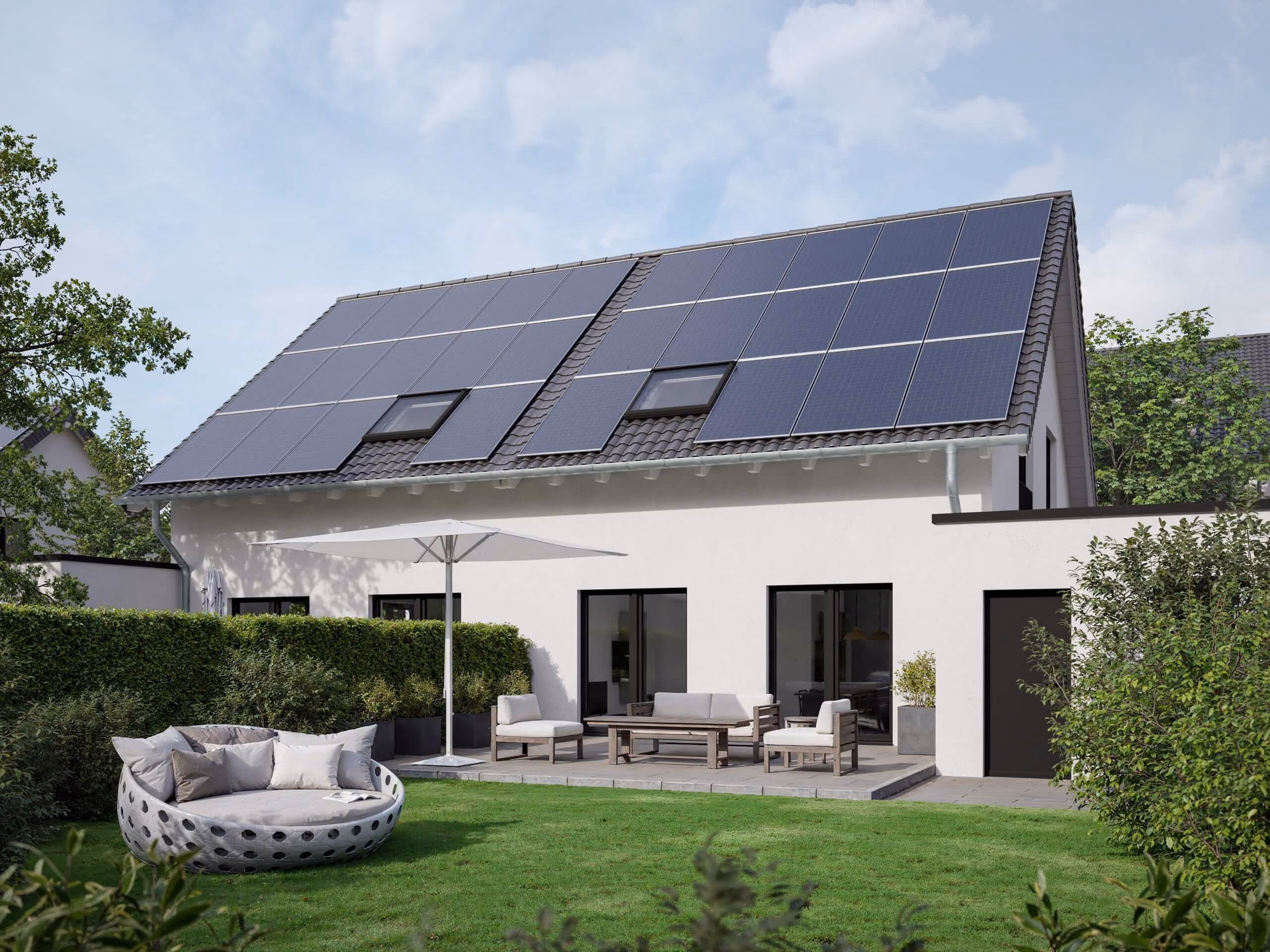 Modern house with solar panels on roof and a patio with seating and umbrella in a green garden.