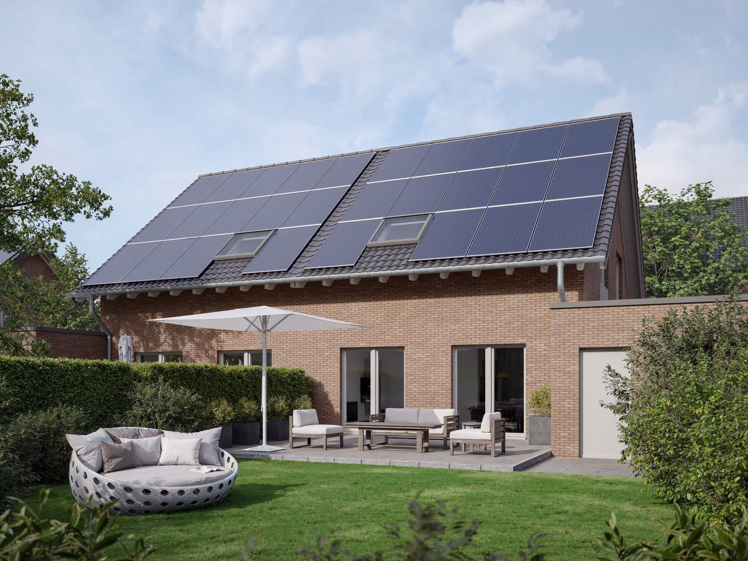 Back view of brick house with solar panels on roof, patio furniture, large umbrella, and green garden.