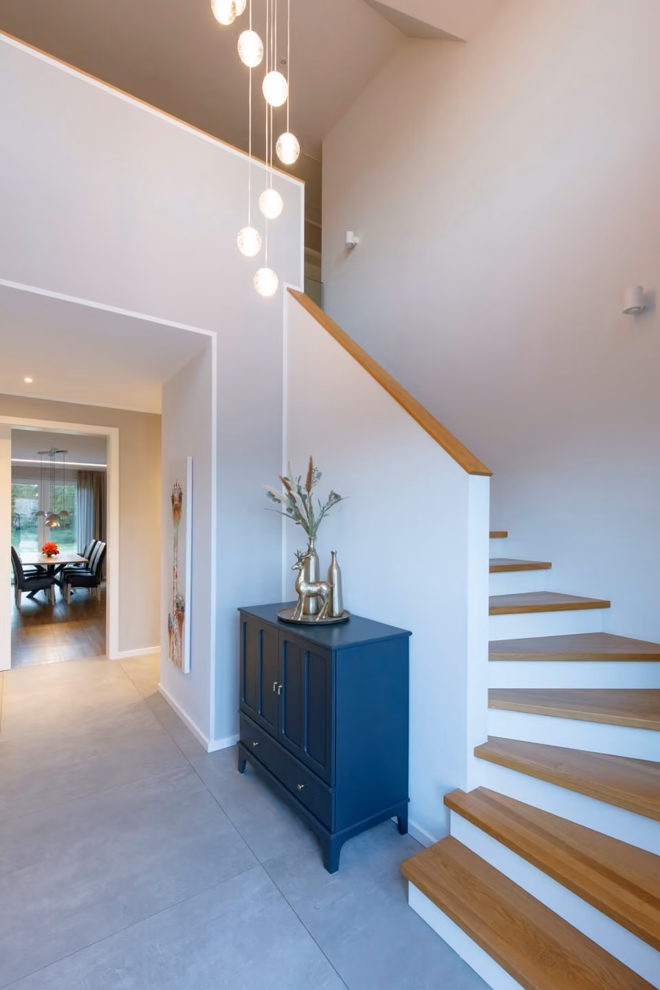 Moderner Eingangsbereich mit Holztreppe, dunklem Sideboard und hängenden Kugelleuchten.