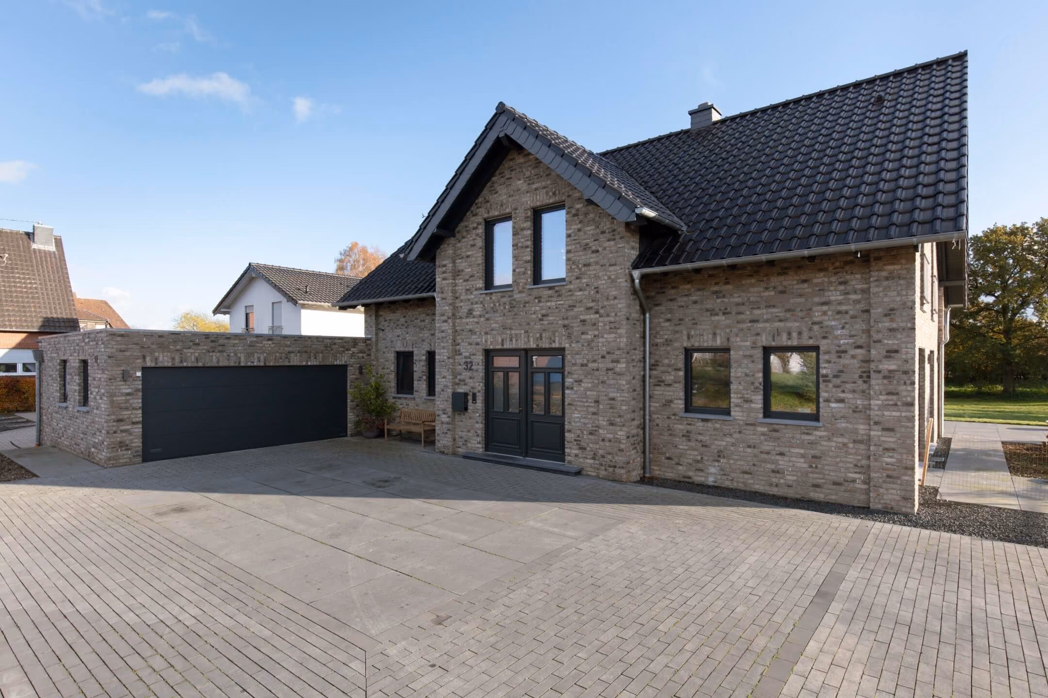 Modernes Haus mit Ziegelfassade, schwarzem Dach und angrenzender Garage unter blauem Himmel.