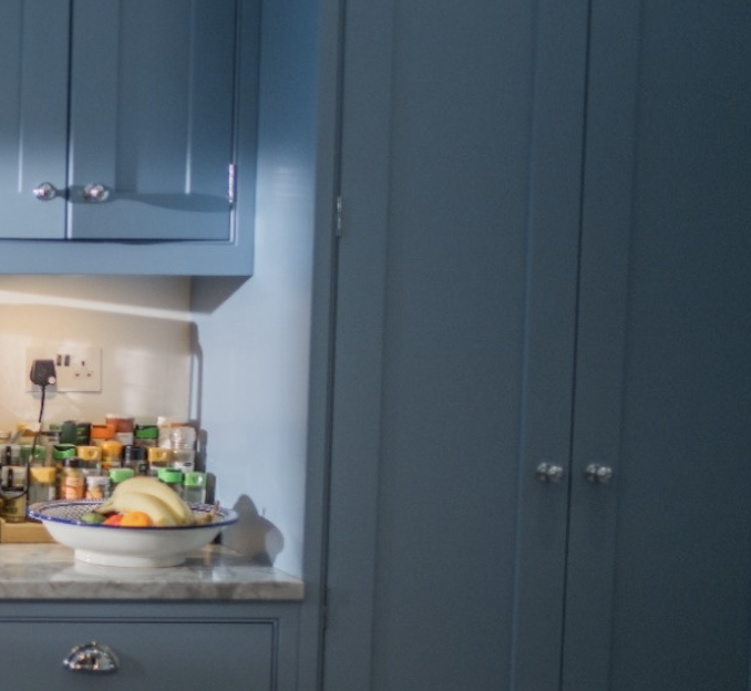 Kitchen counter with blue cabinets, a fruit bowl with bananas, and assorted spice jars near an electric outlet.